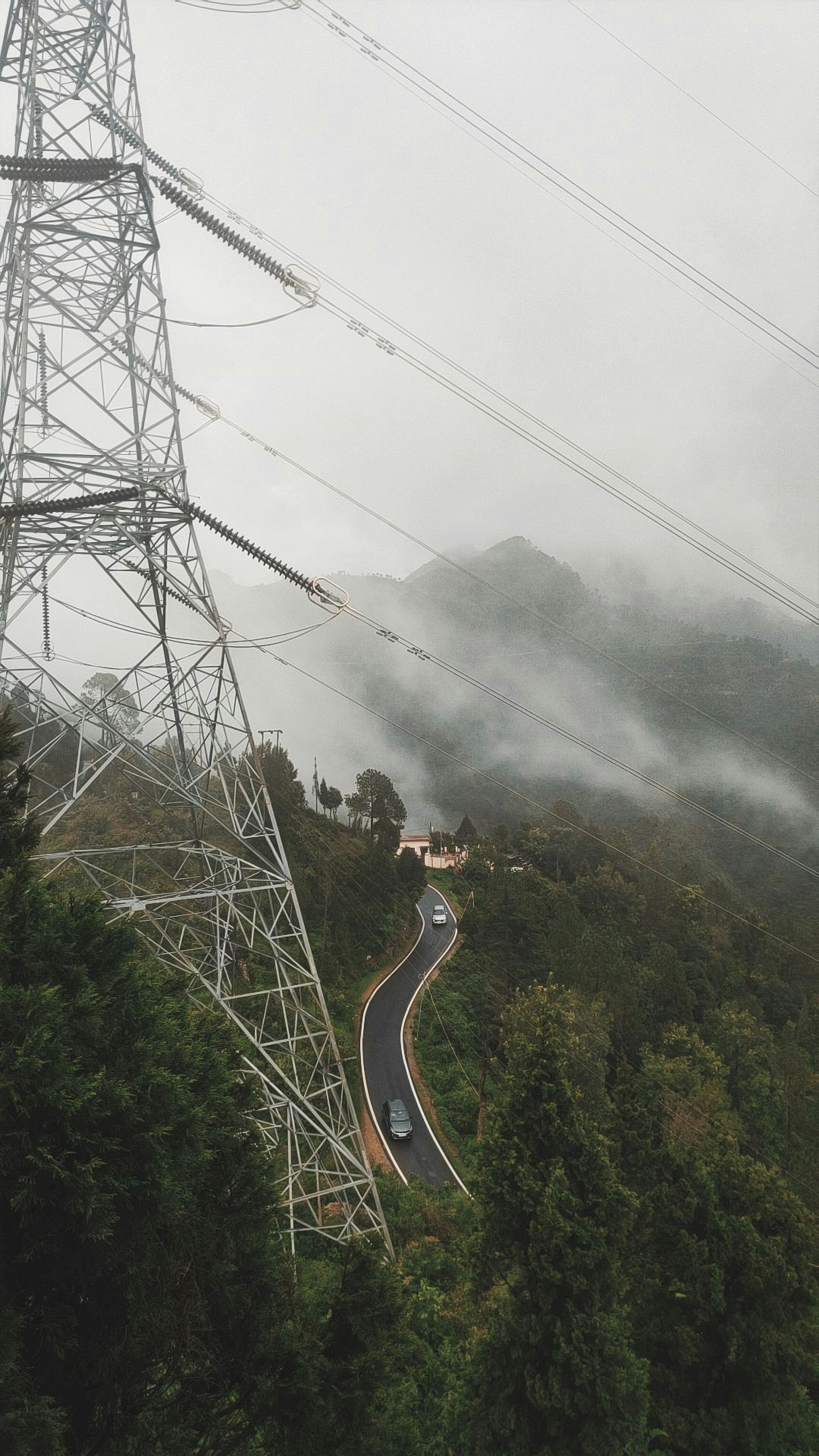 Cars drive on a winding road near a power tower.