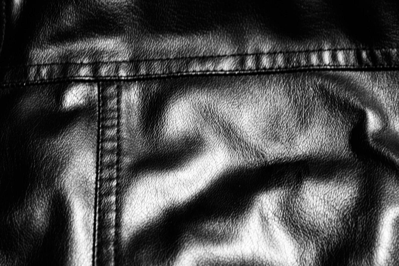 Black leather photographed close, the stitching and needle marks visible.