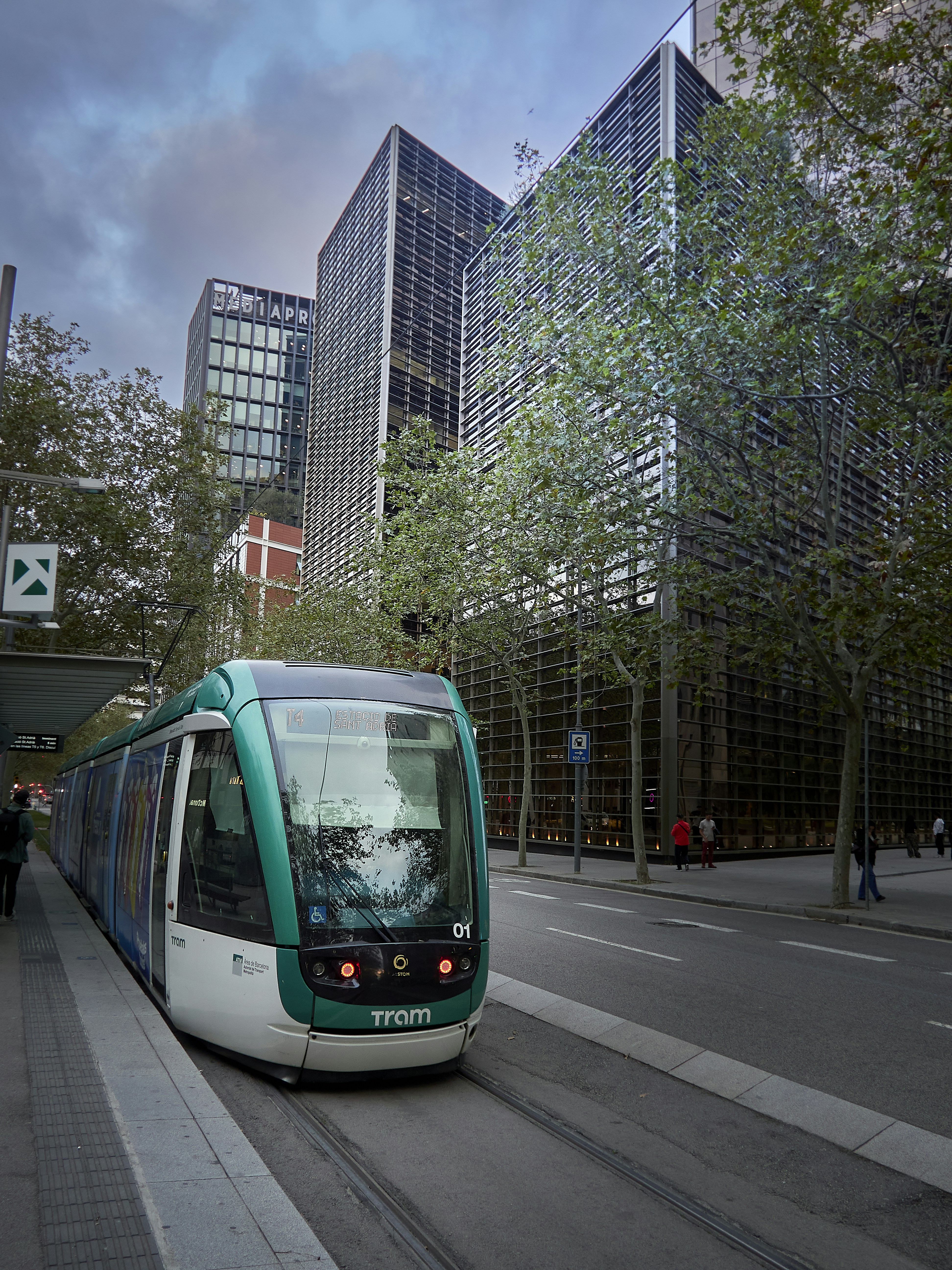 A modern tram passes tall glass buildings on a street.