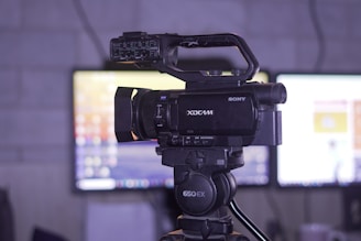 Professional video camera on a tripod with monitors behind