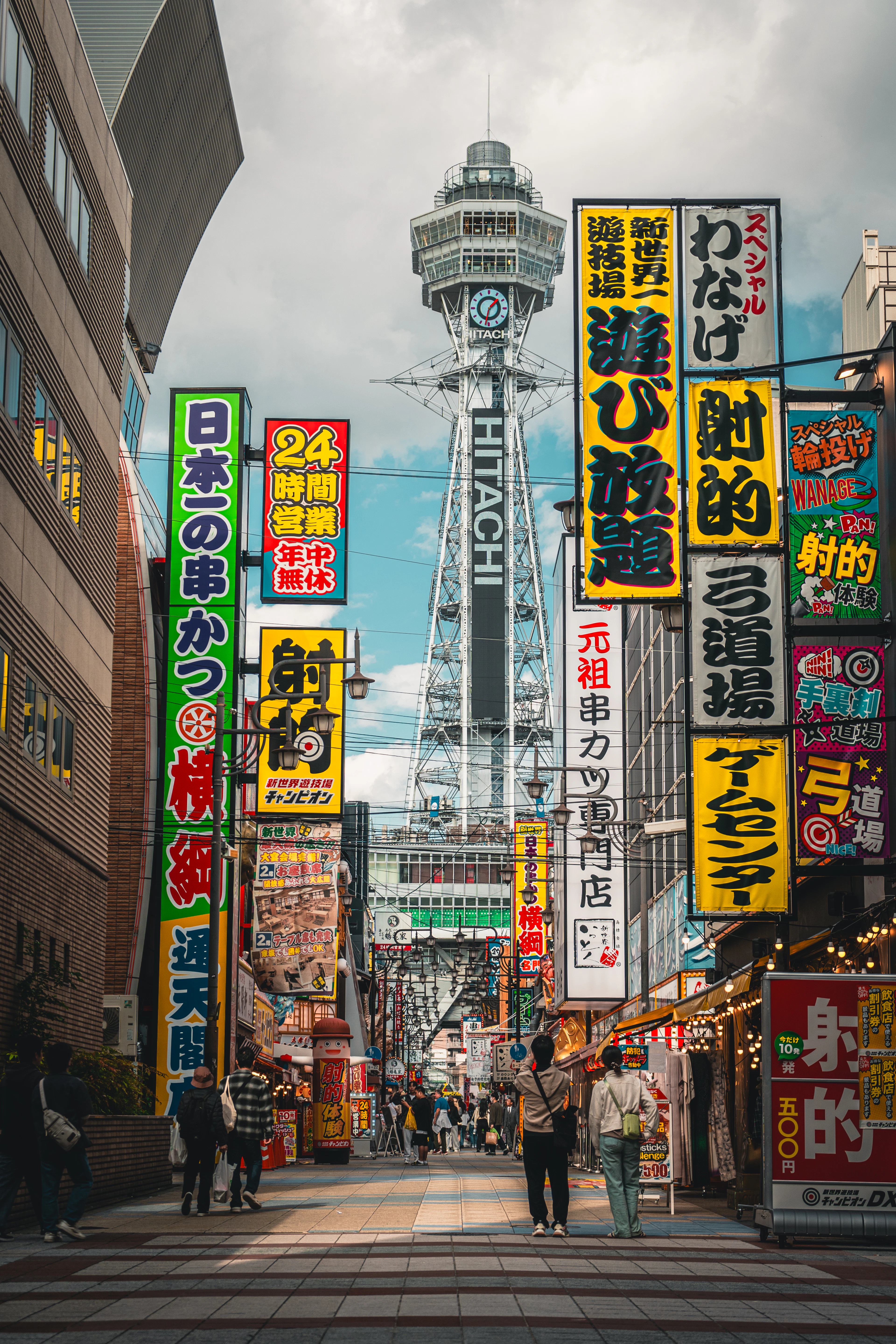 The Tsutenkaku tower seen down a Shinsekai street crowded with tall yellow, green and red Japanese signboards