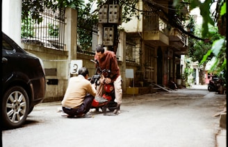 Two people working on a scooter on a street