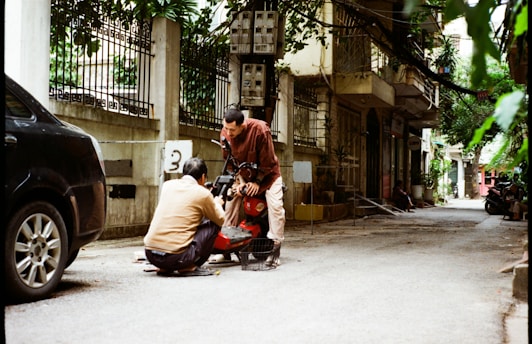 Two people working on a scooter on a street