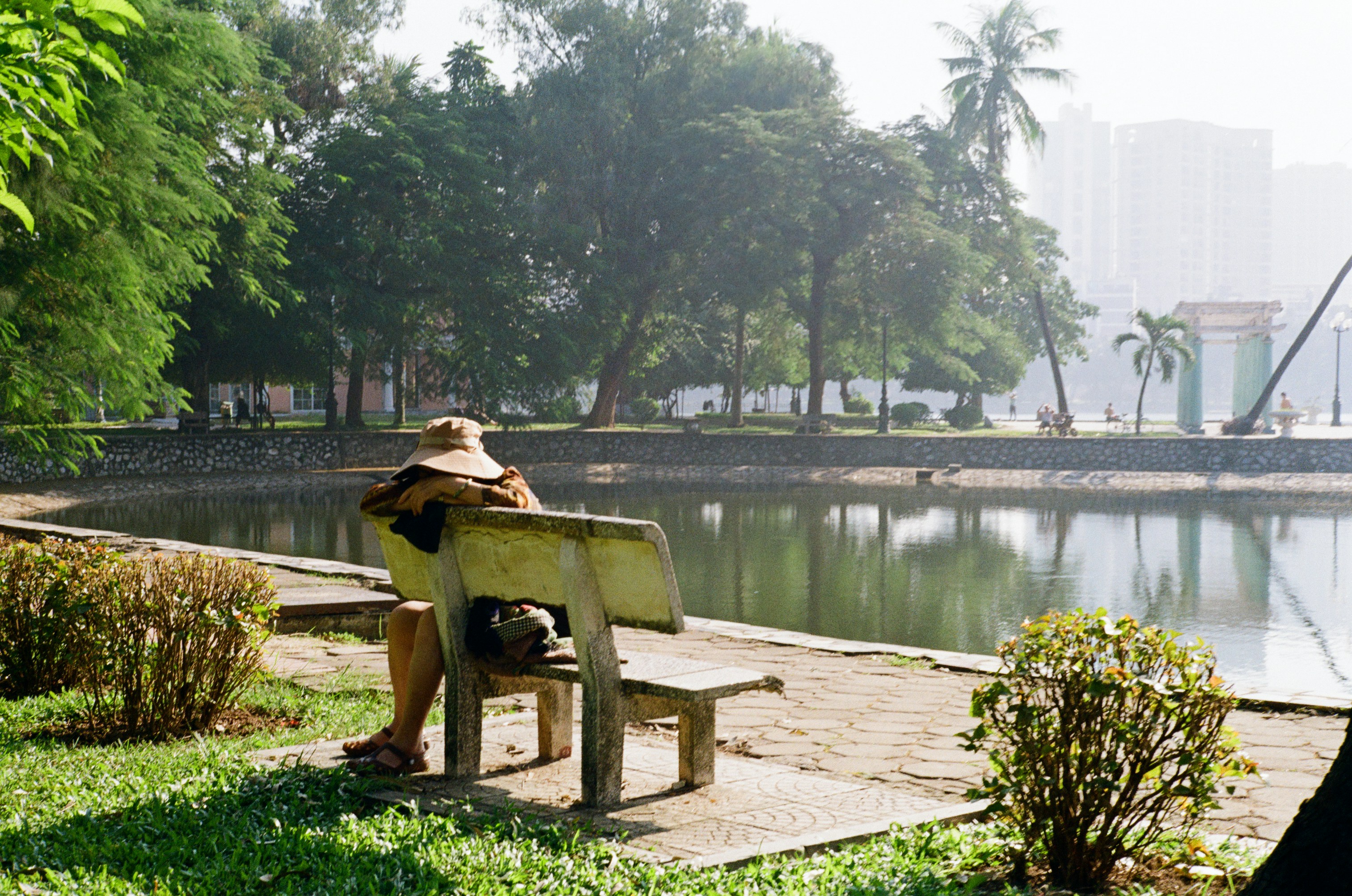 Person in hat sits on park bench by lake.