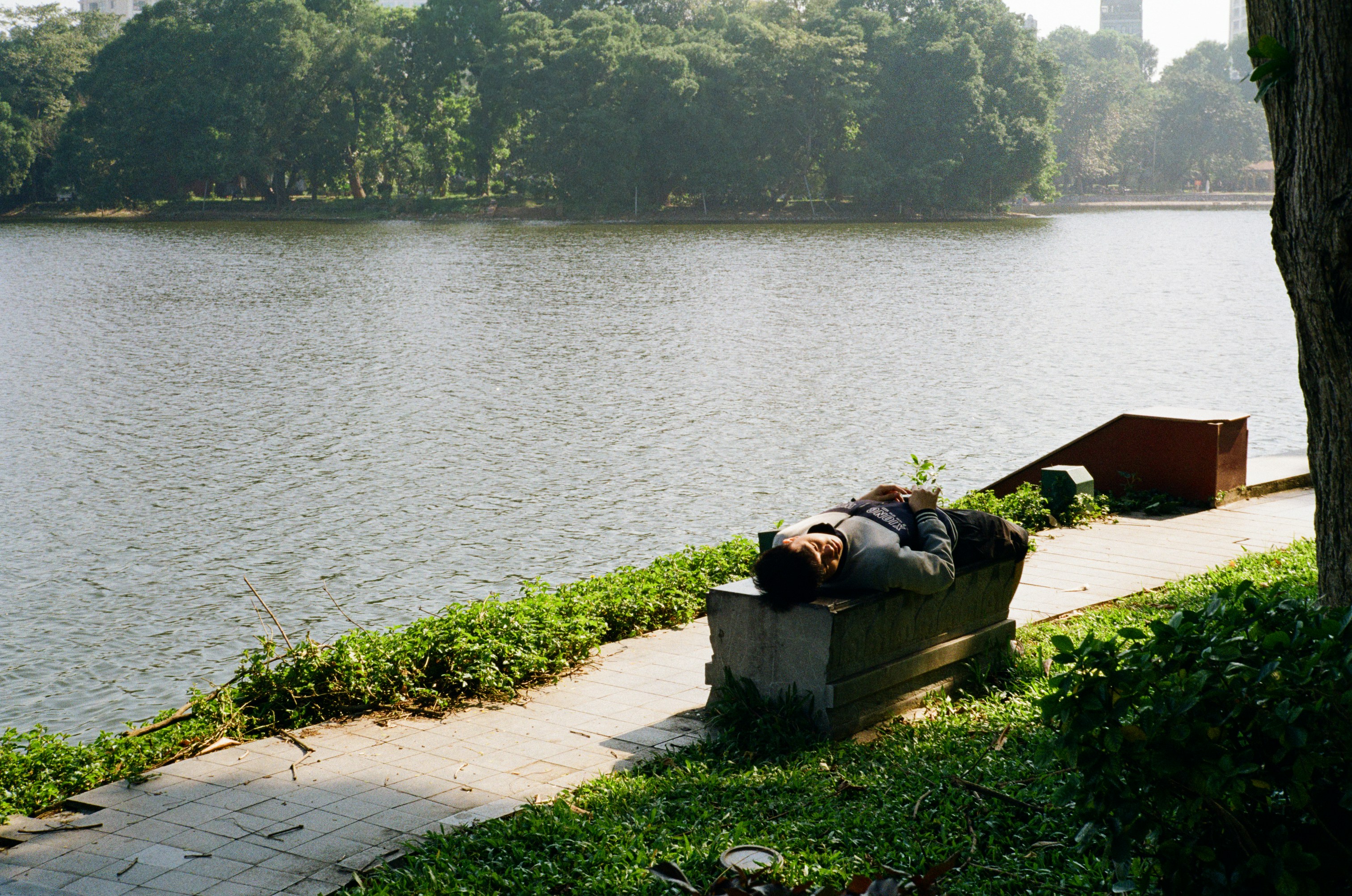 Person sleeping on a bench by the lake.