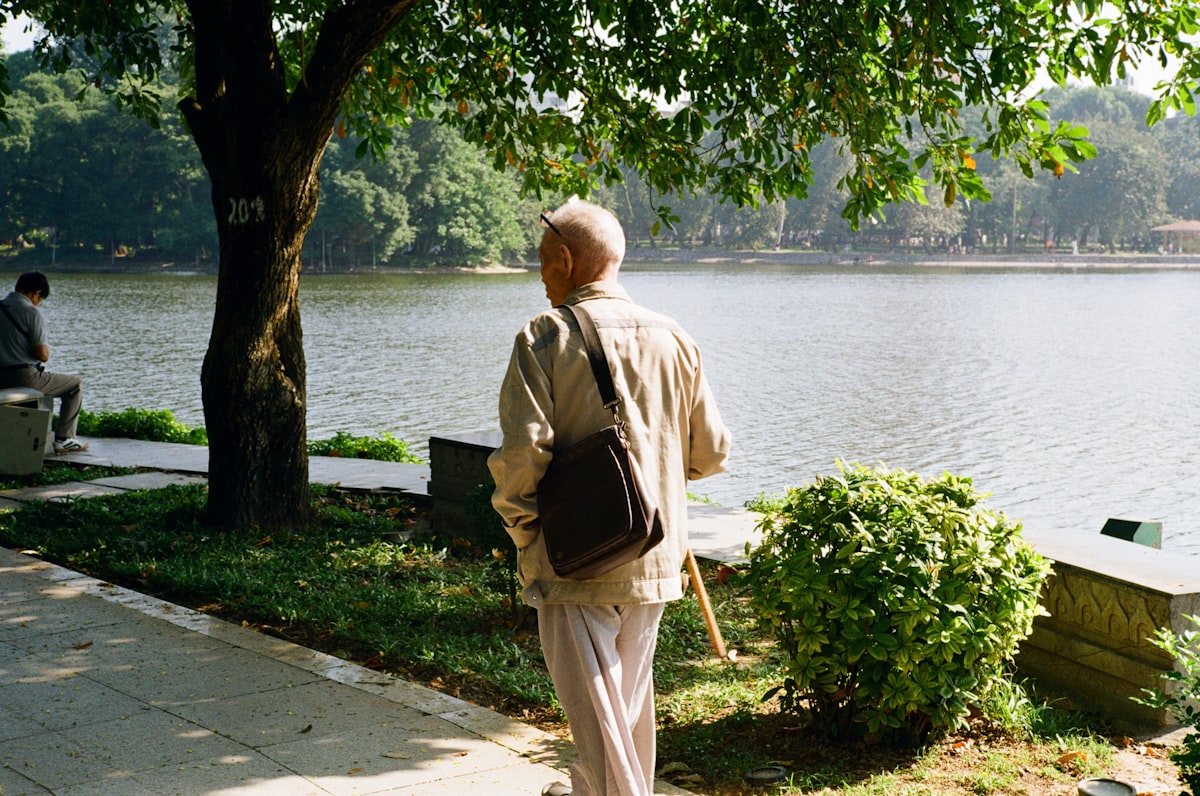 Elderly man with a cane walking by a lake in a park