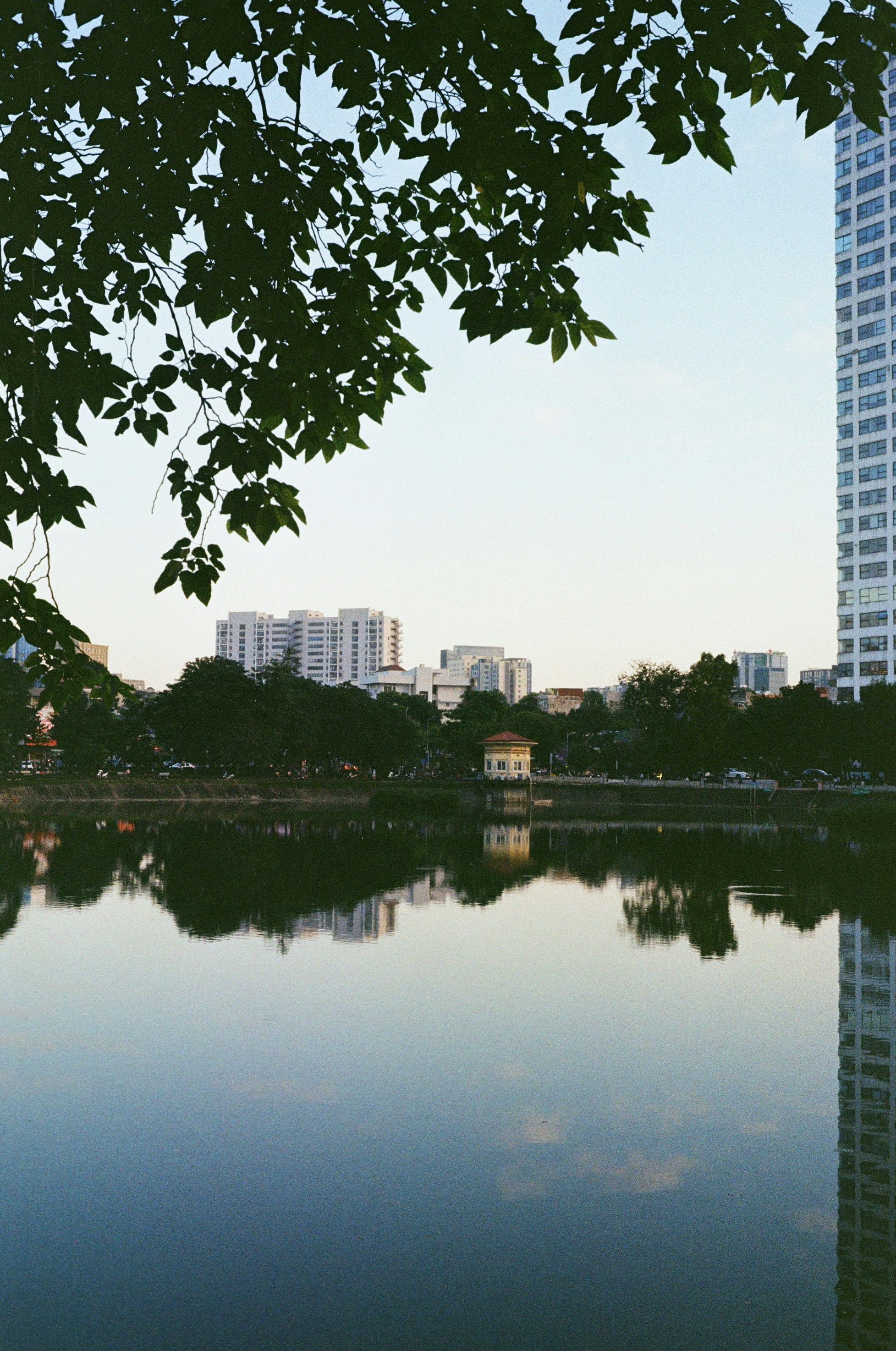 Calm lake reflecting buildings and trees under sky.