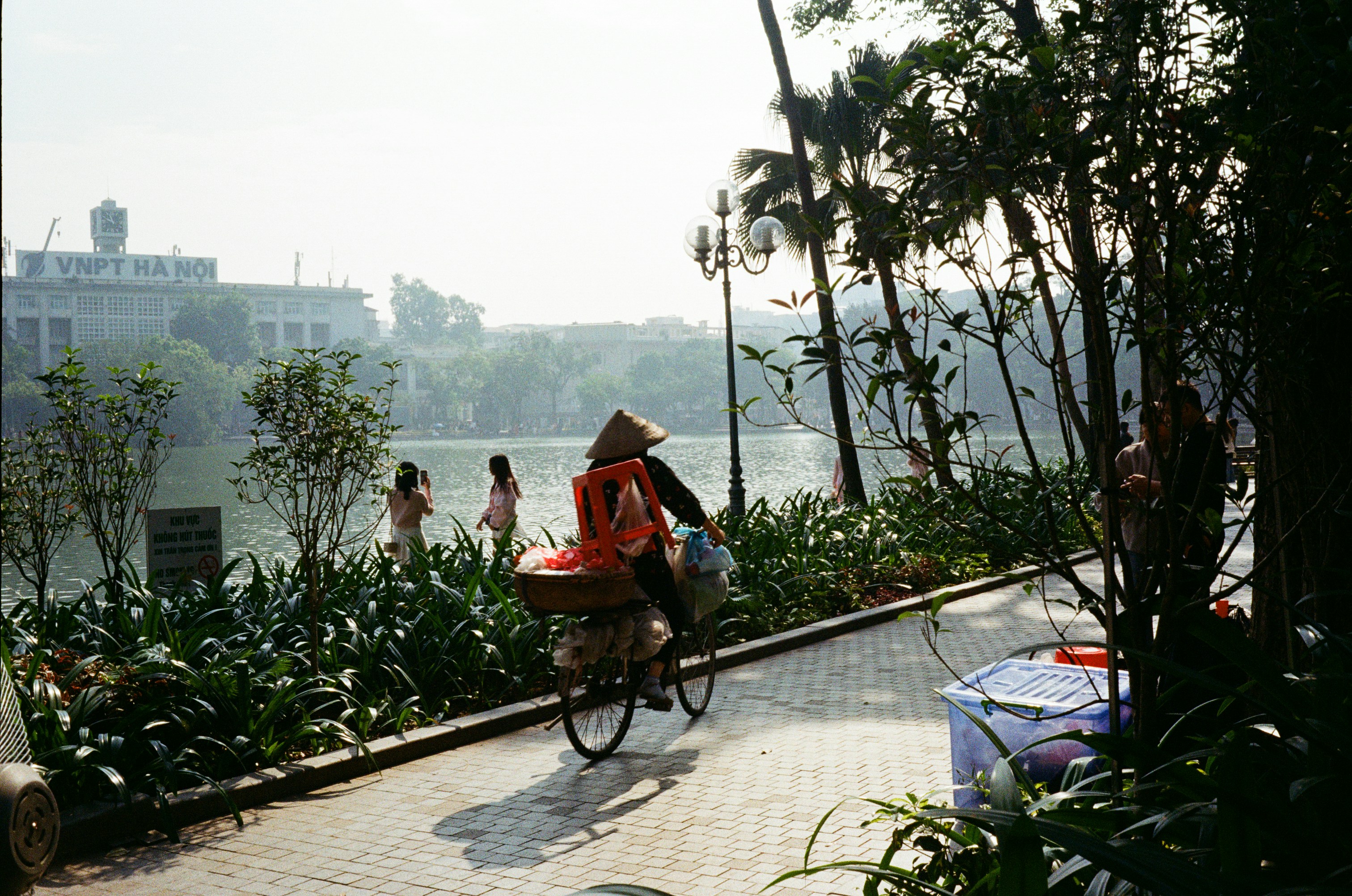 Person riding bicycle with goods near a lake.