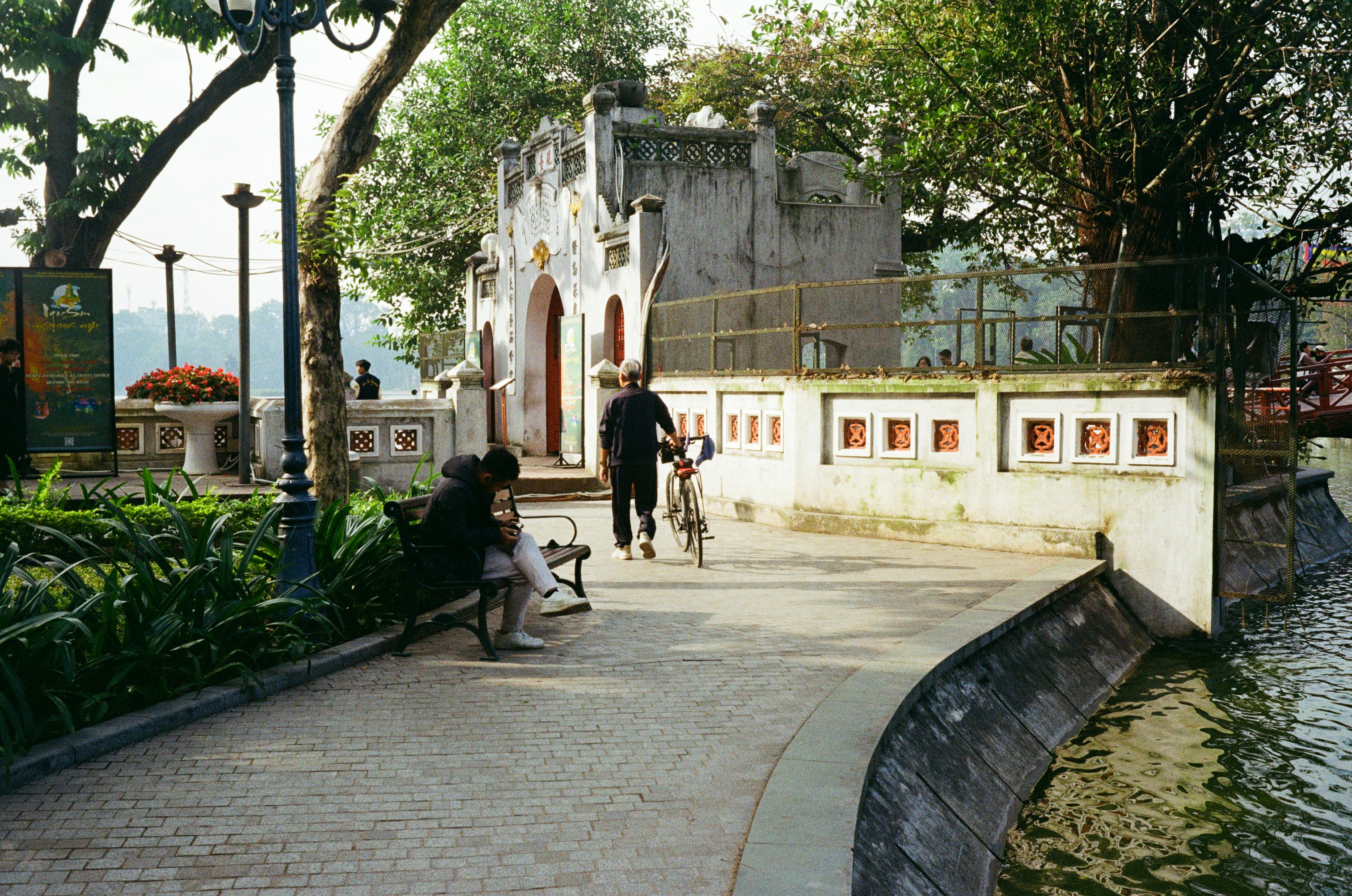 People walking by a lake near an old building.