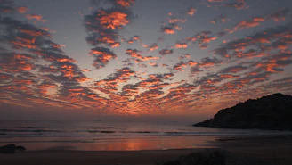 Dramatic sunset clouds over a calm ocean and beach.