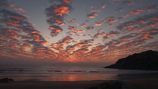 Dramatic sunset clouds over a calm ocean and beach.