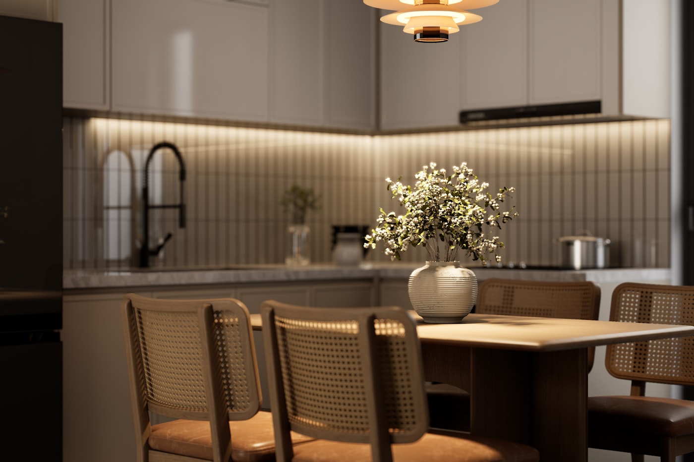Warm apartment kitchen dining nook with rattan cane chairs, wood dining table, warm pendant light, and white kitchen cabinetry creating a cozy earth tone dining space