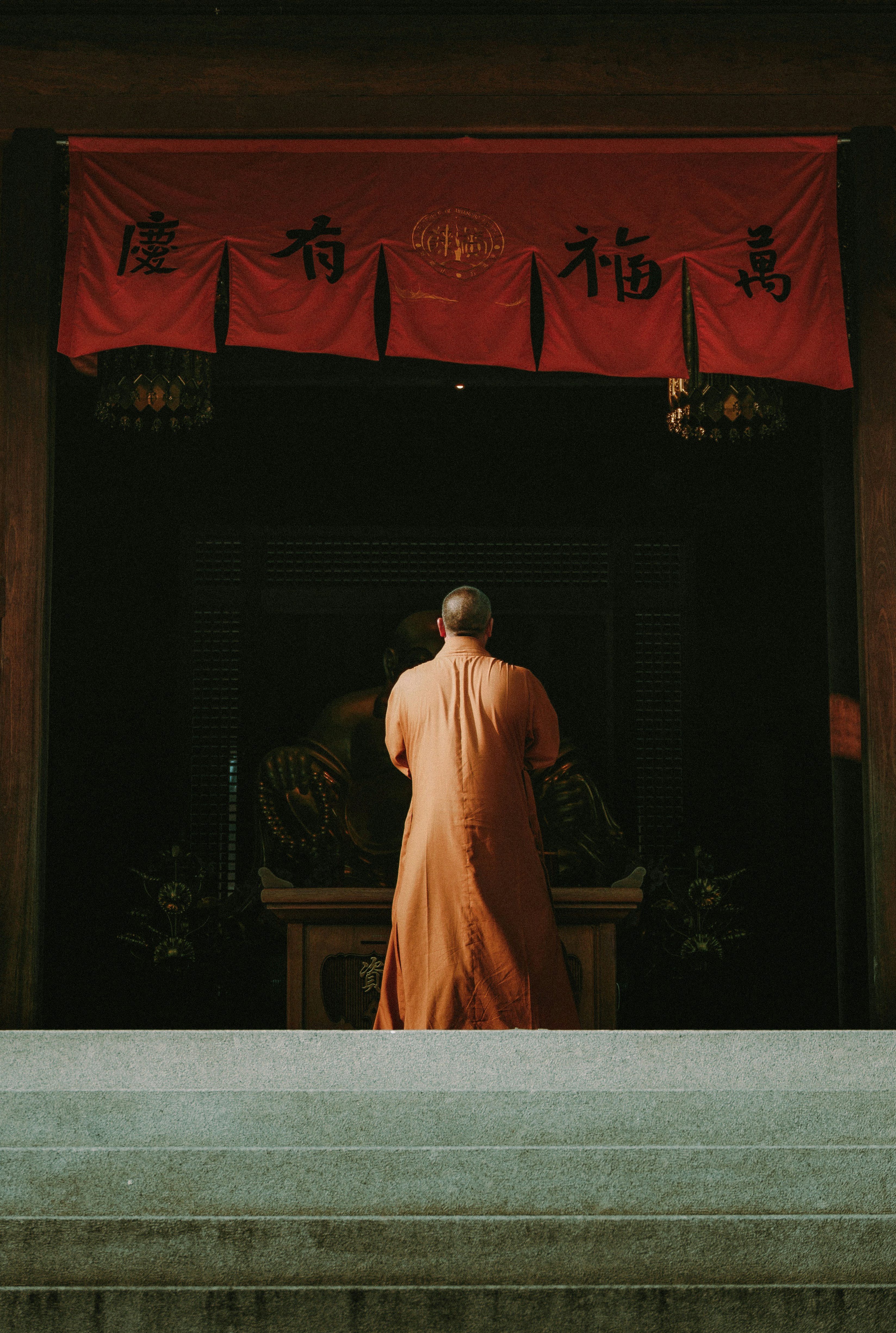 Monk praying inside a temple with red banners.