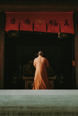 Monk praying inside a temple with red banners.