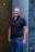 A smiling man in a dark polo shirt and jeans.