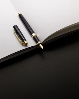 A black and gold pen rests on an open notebook.