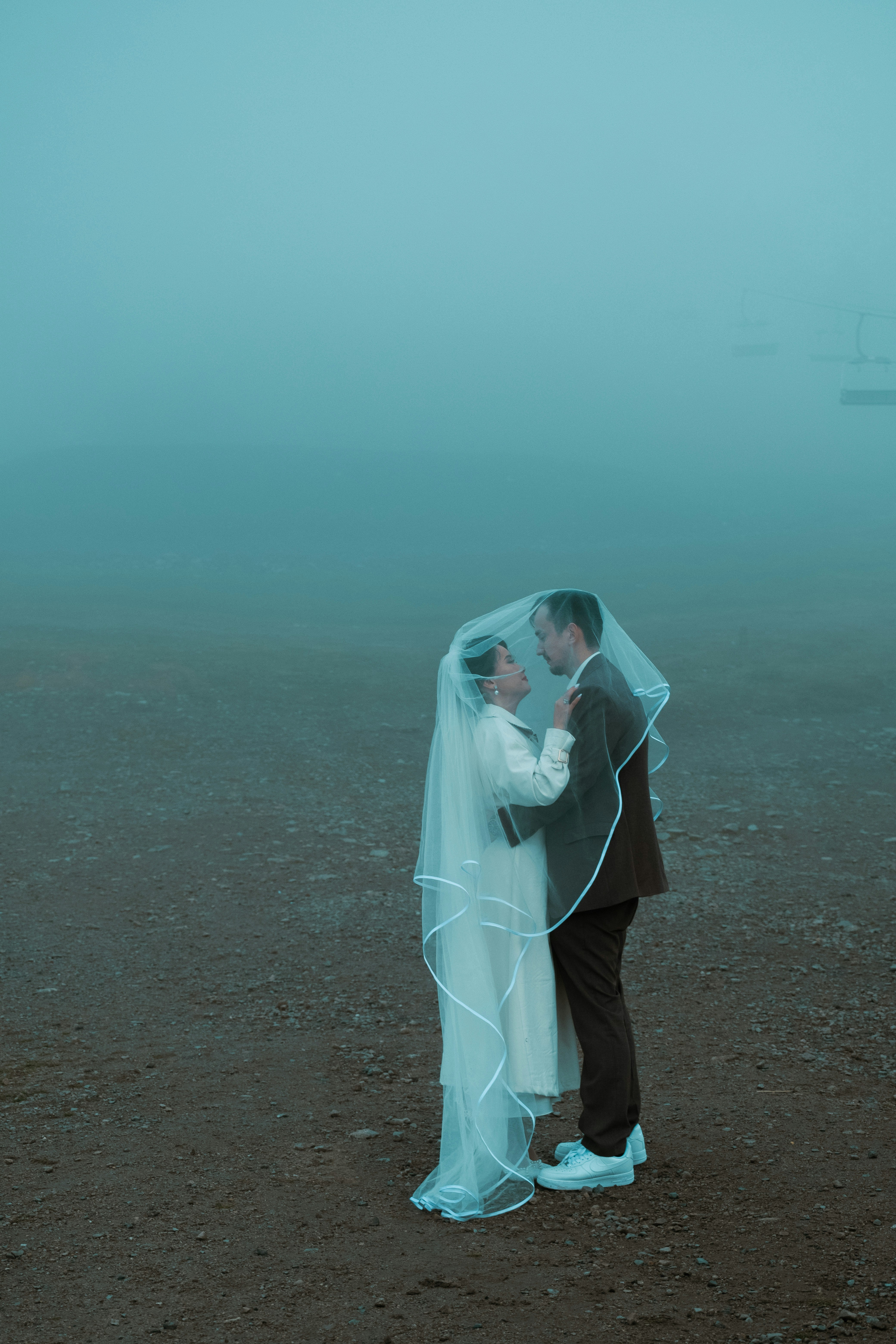 Braut und Bräutigam umarmen sich unter einem Schleier im Nebel.