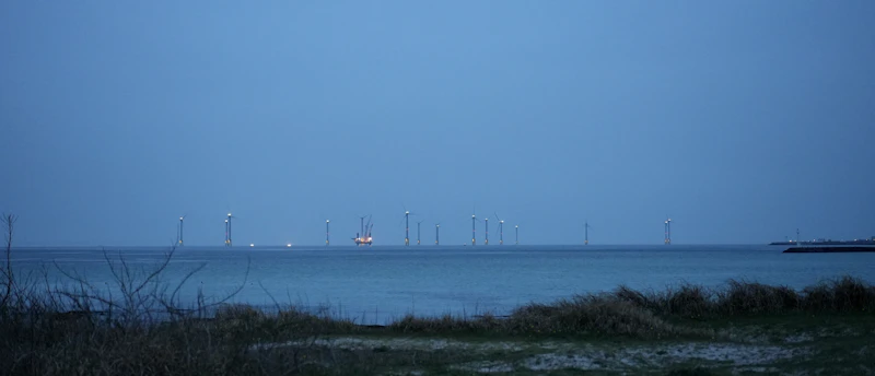 Offshore wind turbines standing in distant ocean under overcast sky