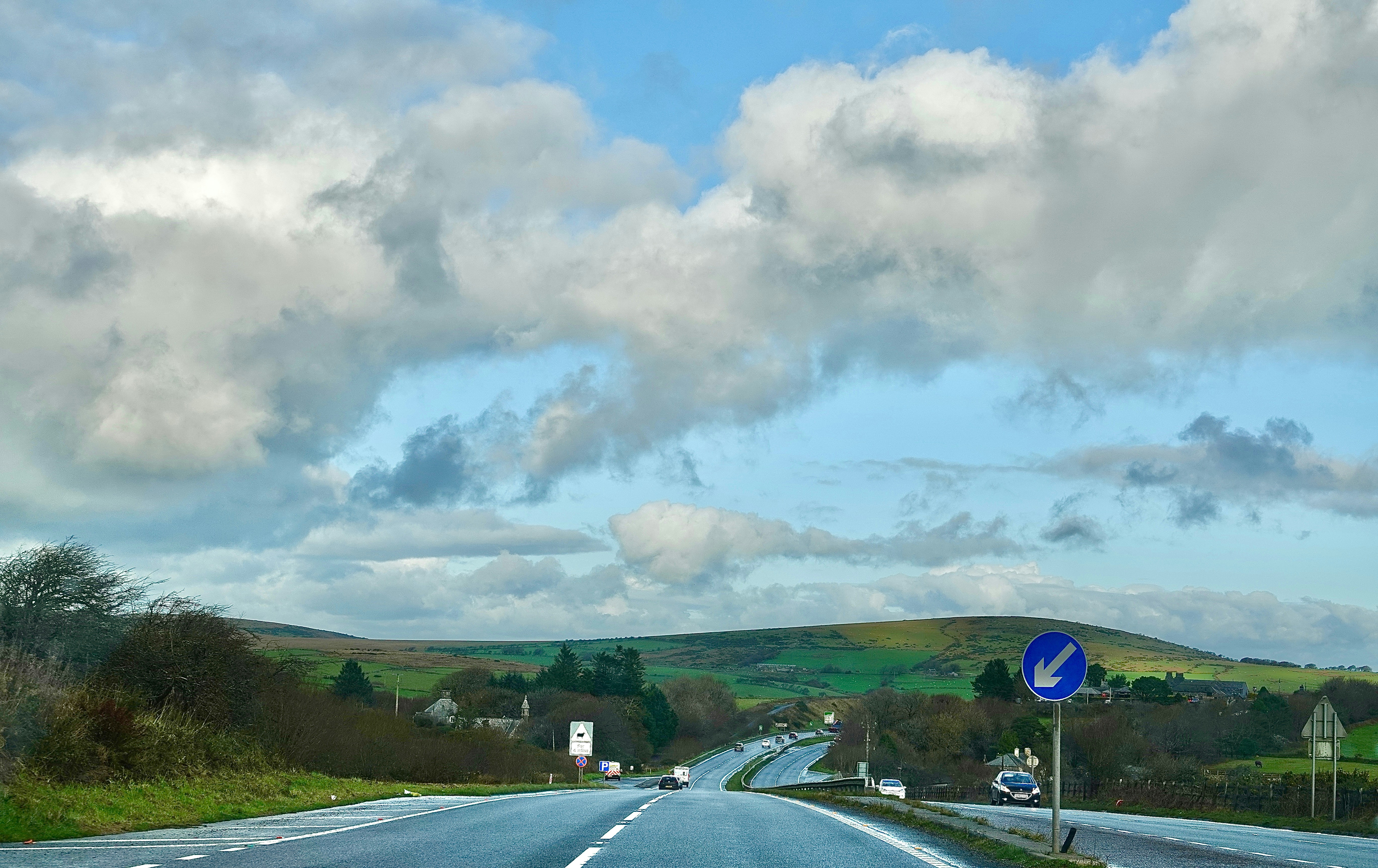 Road leading through rolling green hills under cloudy sky