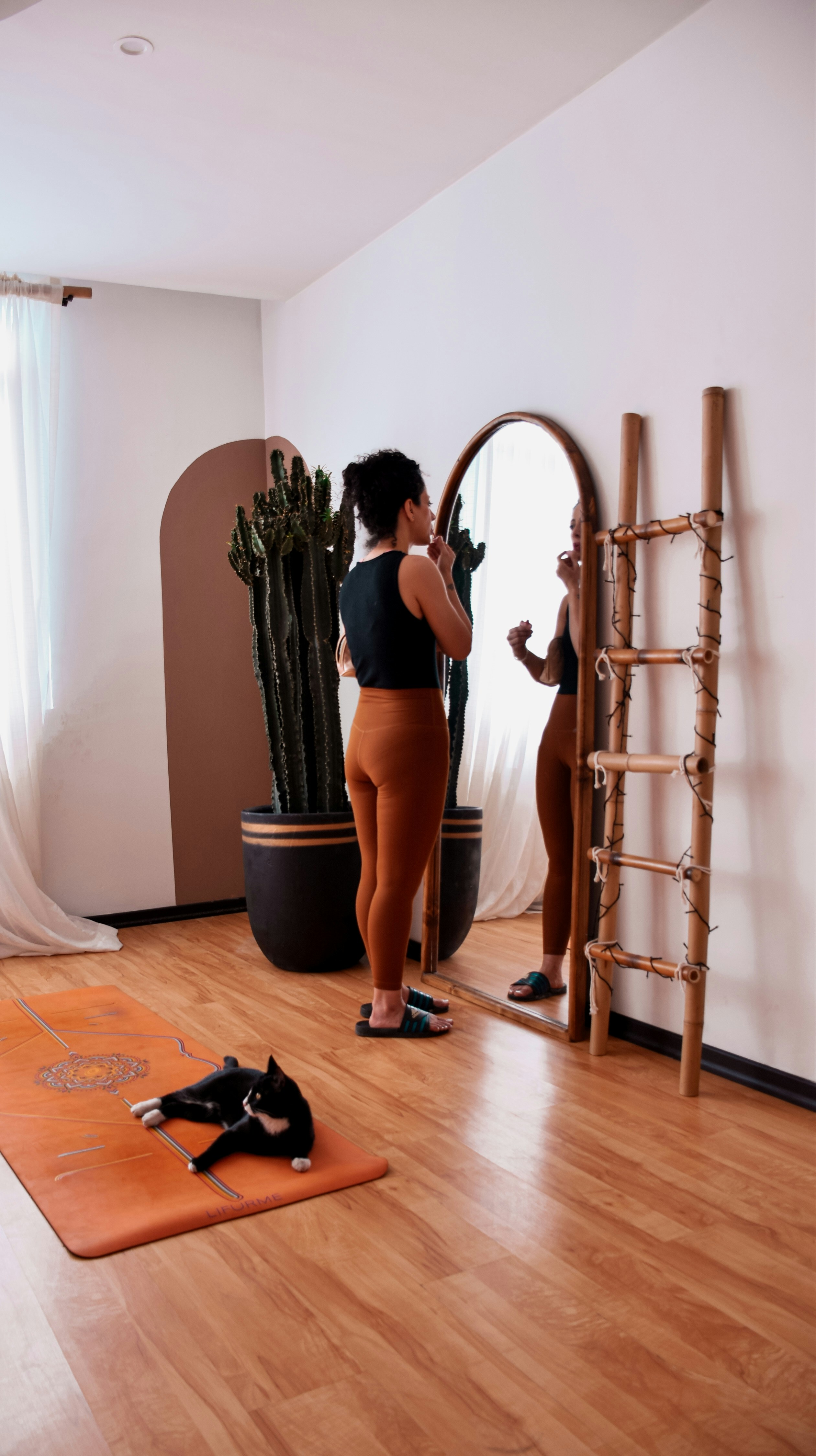 Woman applying makeup in a mirror with cat nearby.
