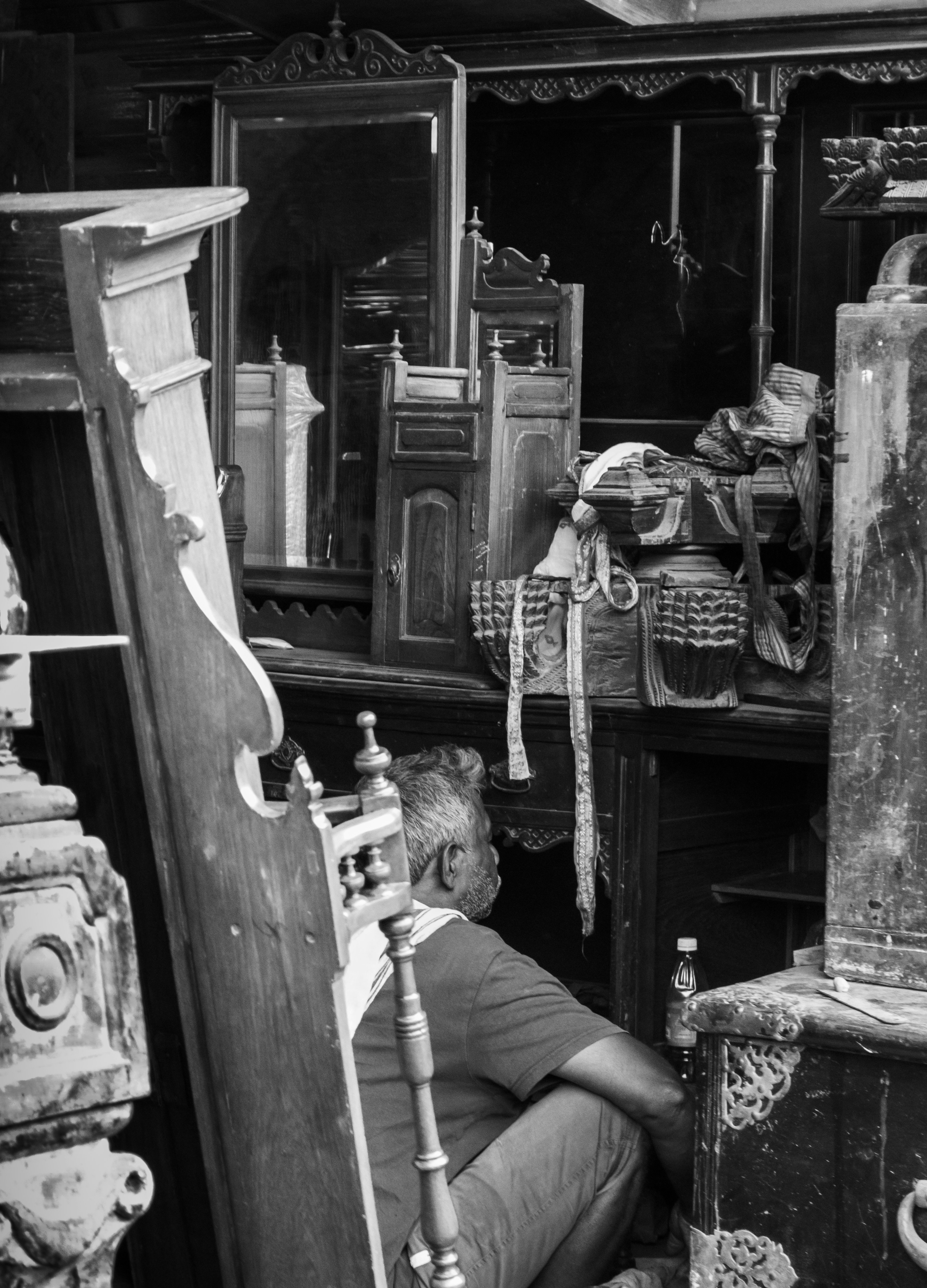 Person examining antique furniture in a cluttered shop.
