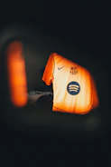 Orange soccer jersey with team crest and sponsor logos.