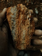 Hand holding a rough, reddish-brown mineral specimen.