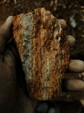 Hand holding a rough, reddish-brown mineral specimen.