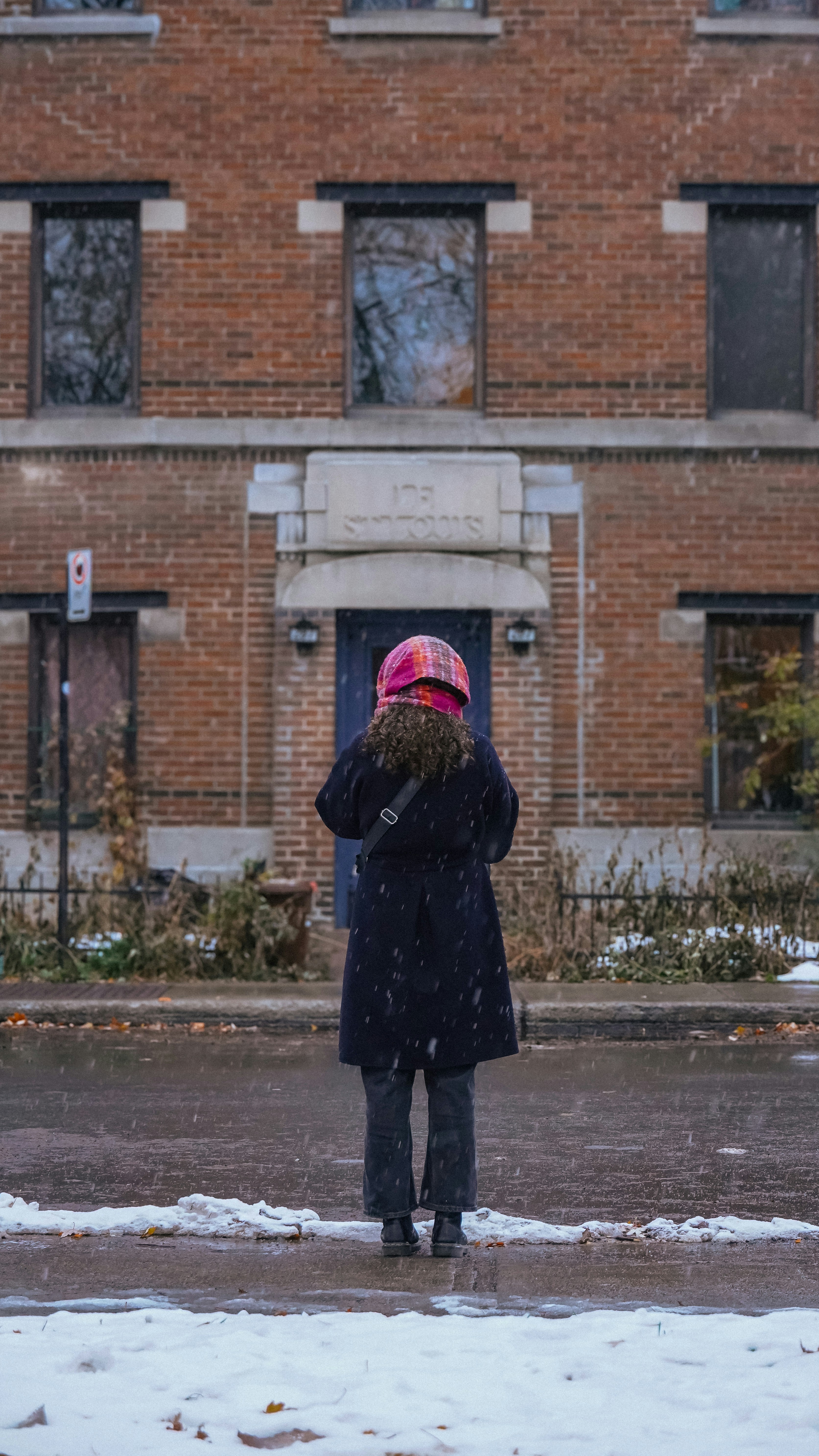 Person in winter coat standing in front of brick building