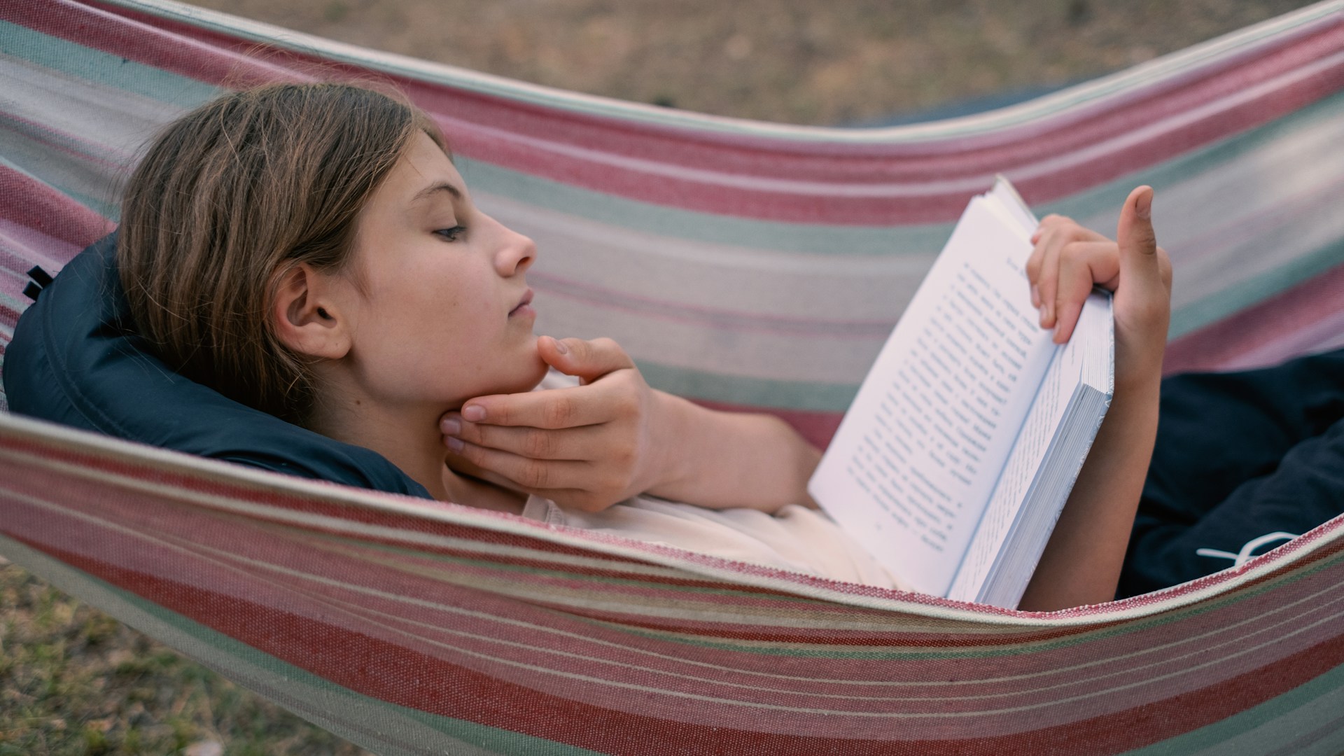 Young girl reading a book in a hammock.