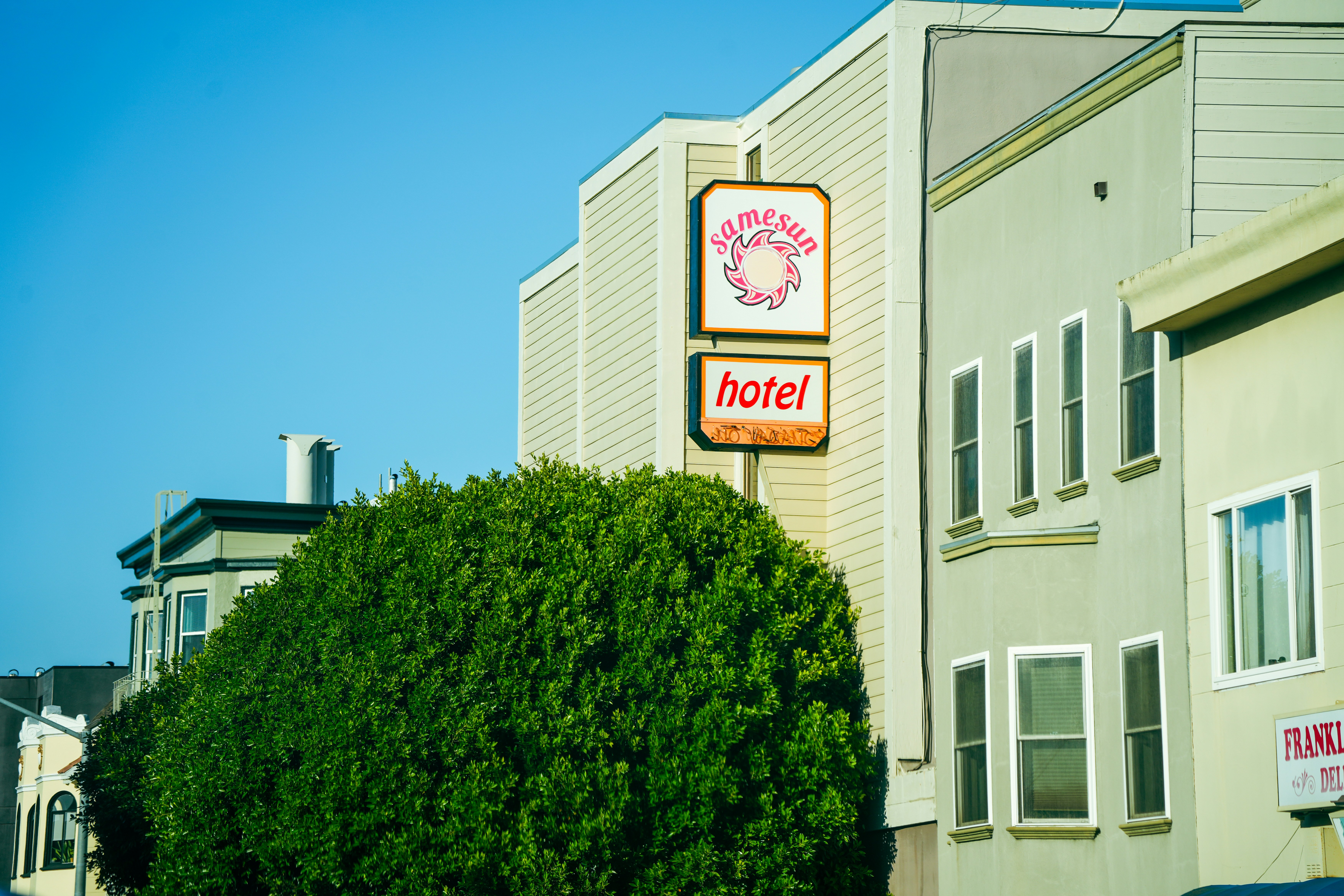 Hotel sign with a large green bush in front.