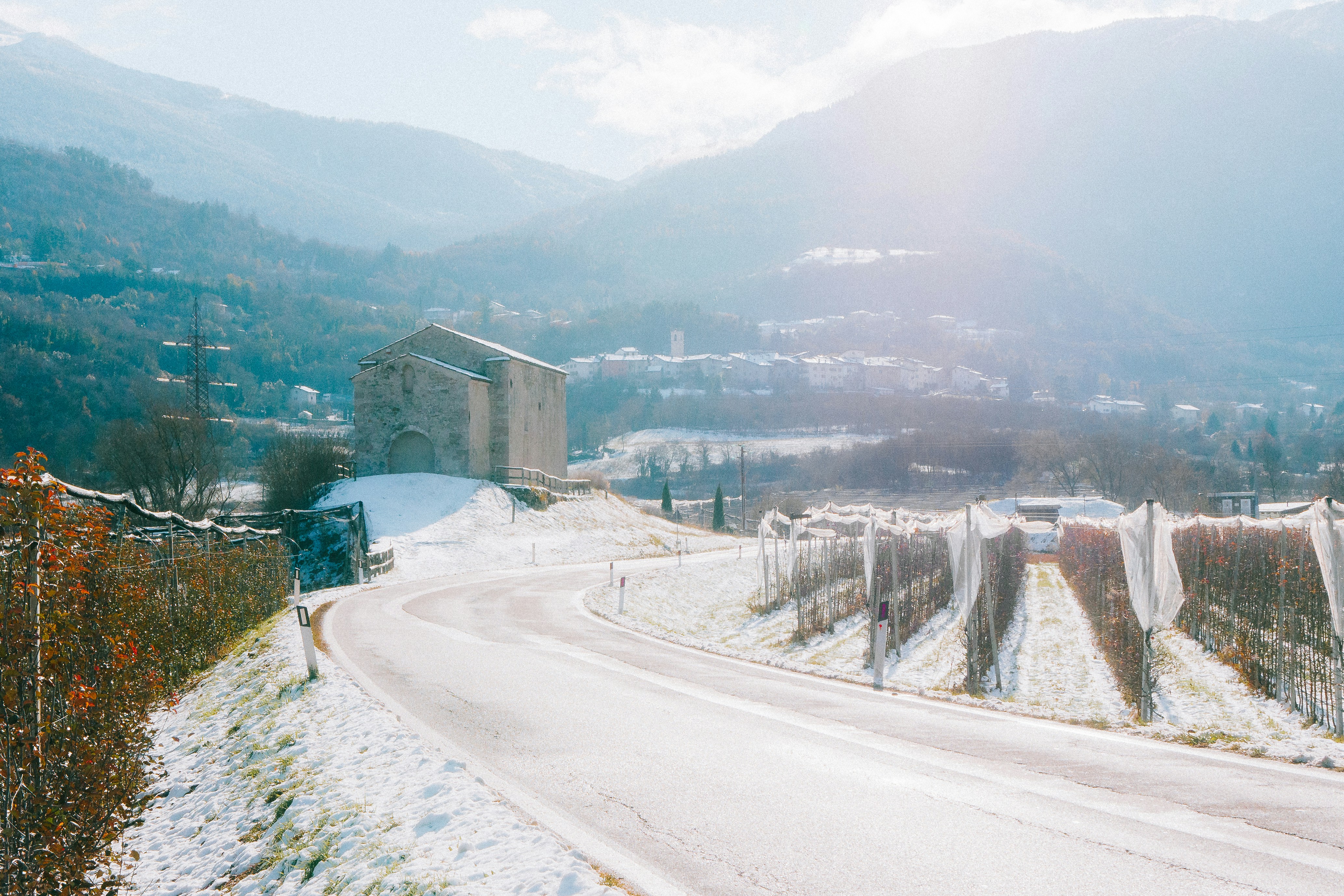 Winding road through snowy landscape with vineyard and building.