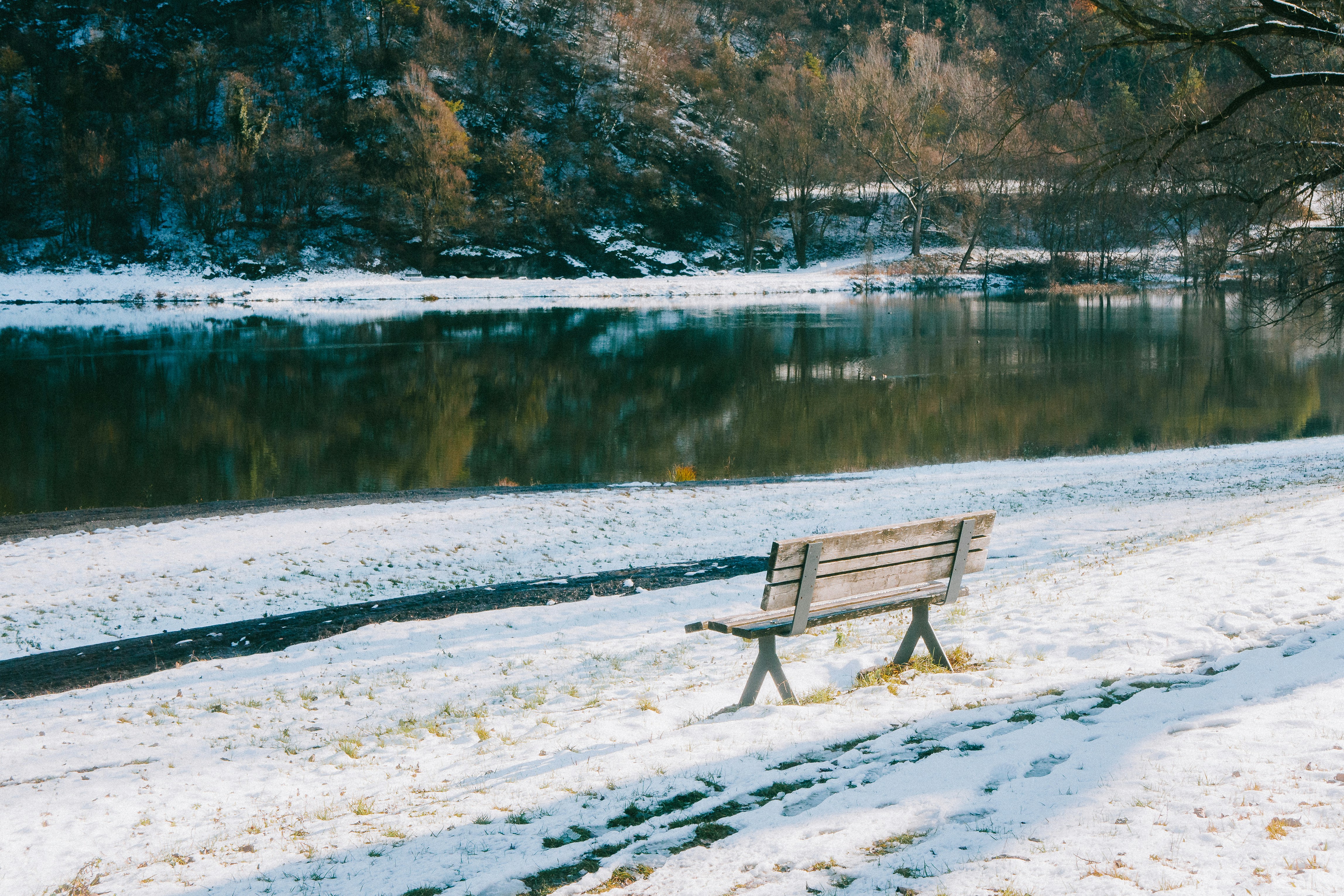 A wooden bench sits by a river in winter.