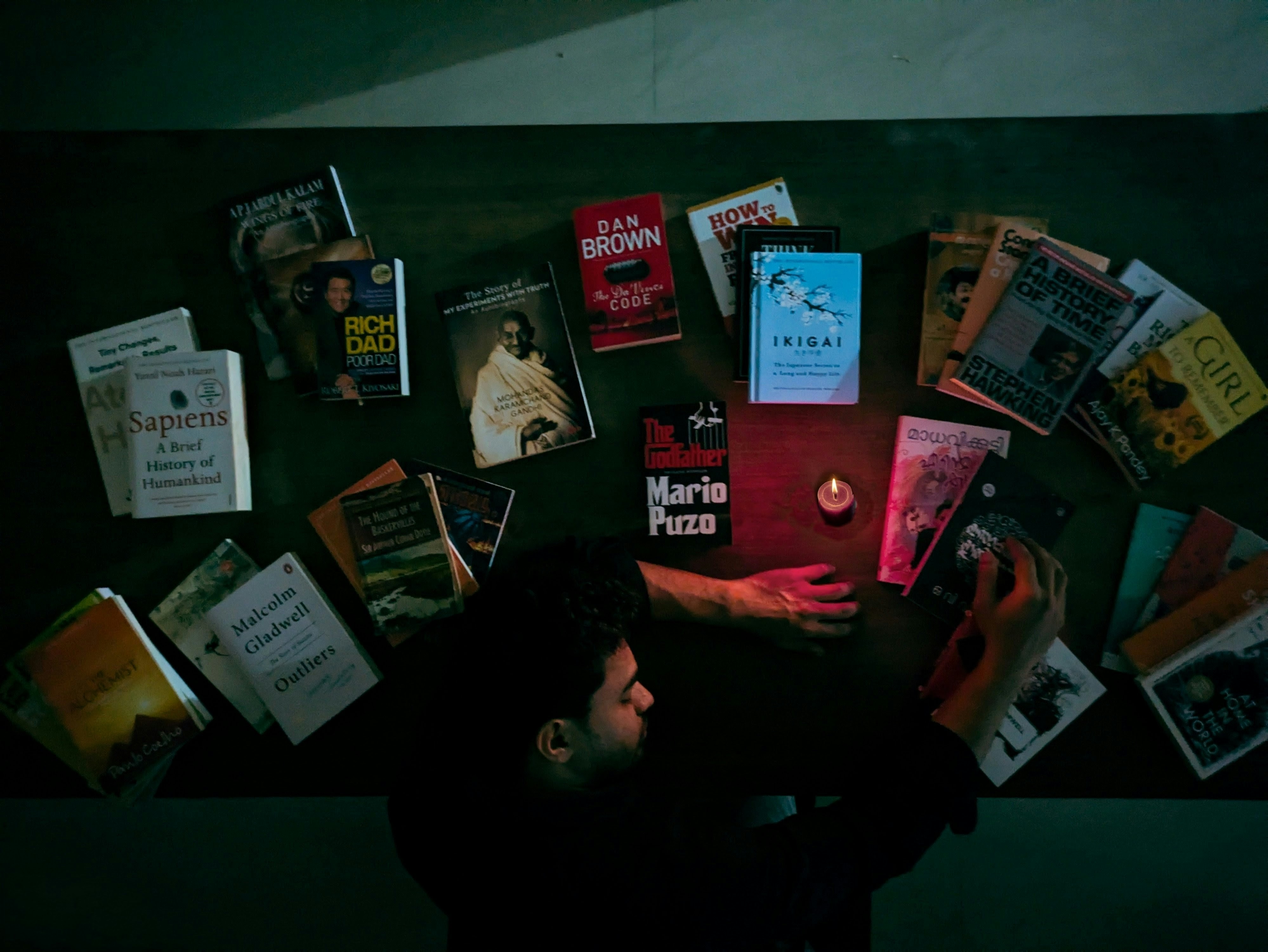 A man at a dark table surrounded by books and a lit candle