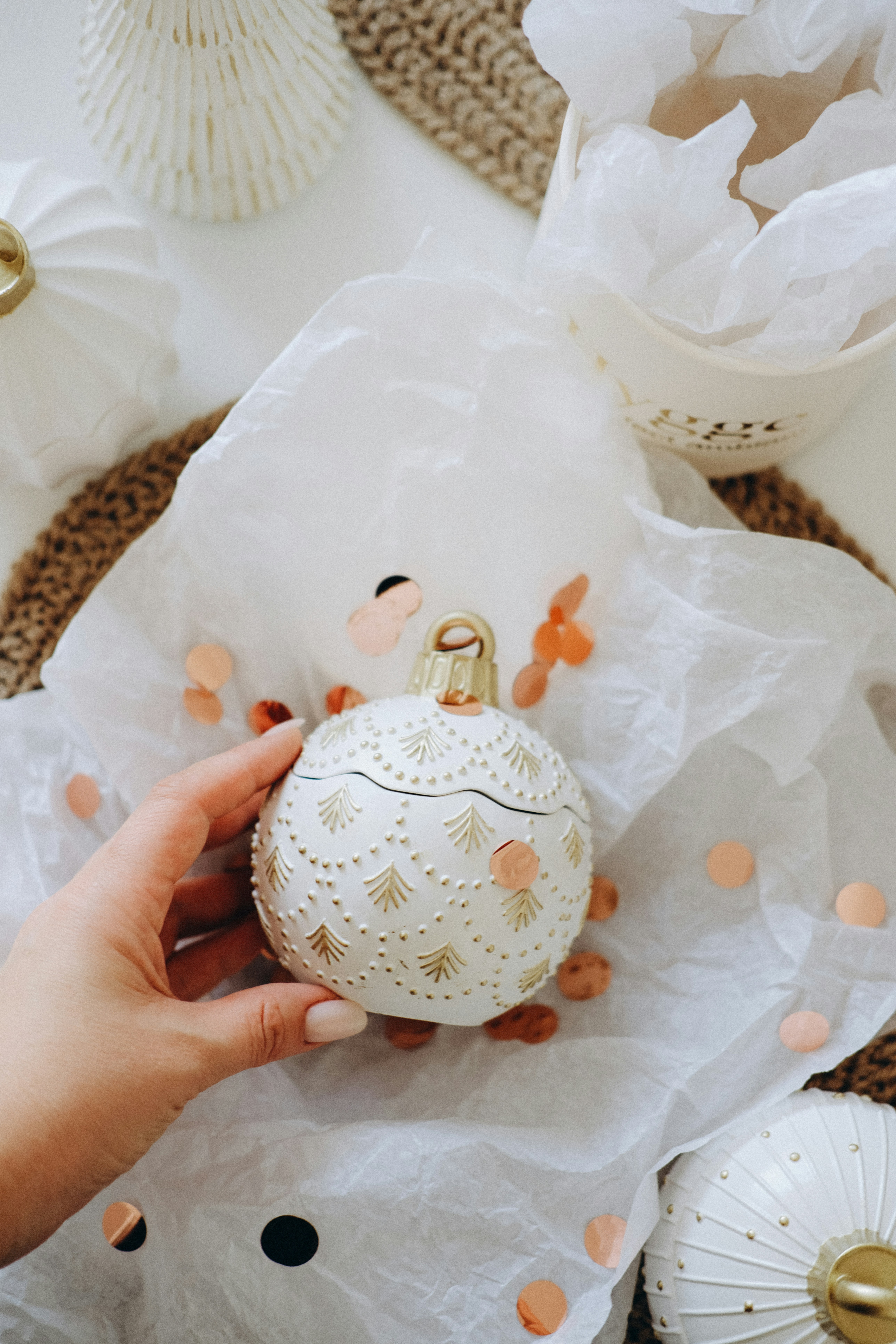 Hand holding decorative white bauble with gold accents