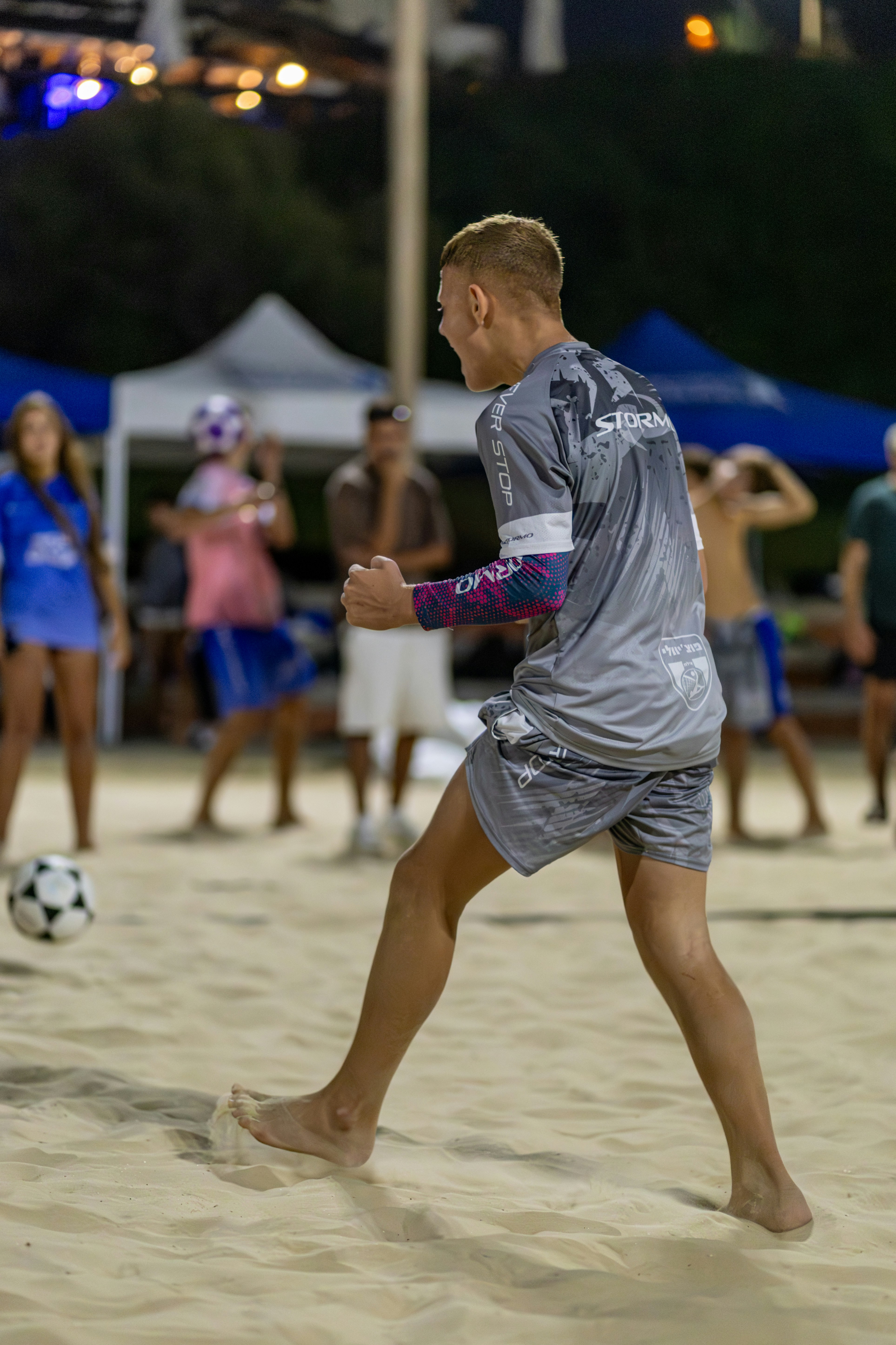 Young man playing soccer on a sandy beach.