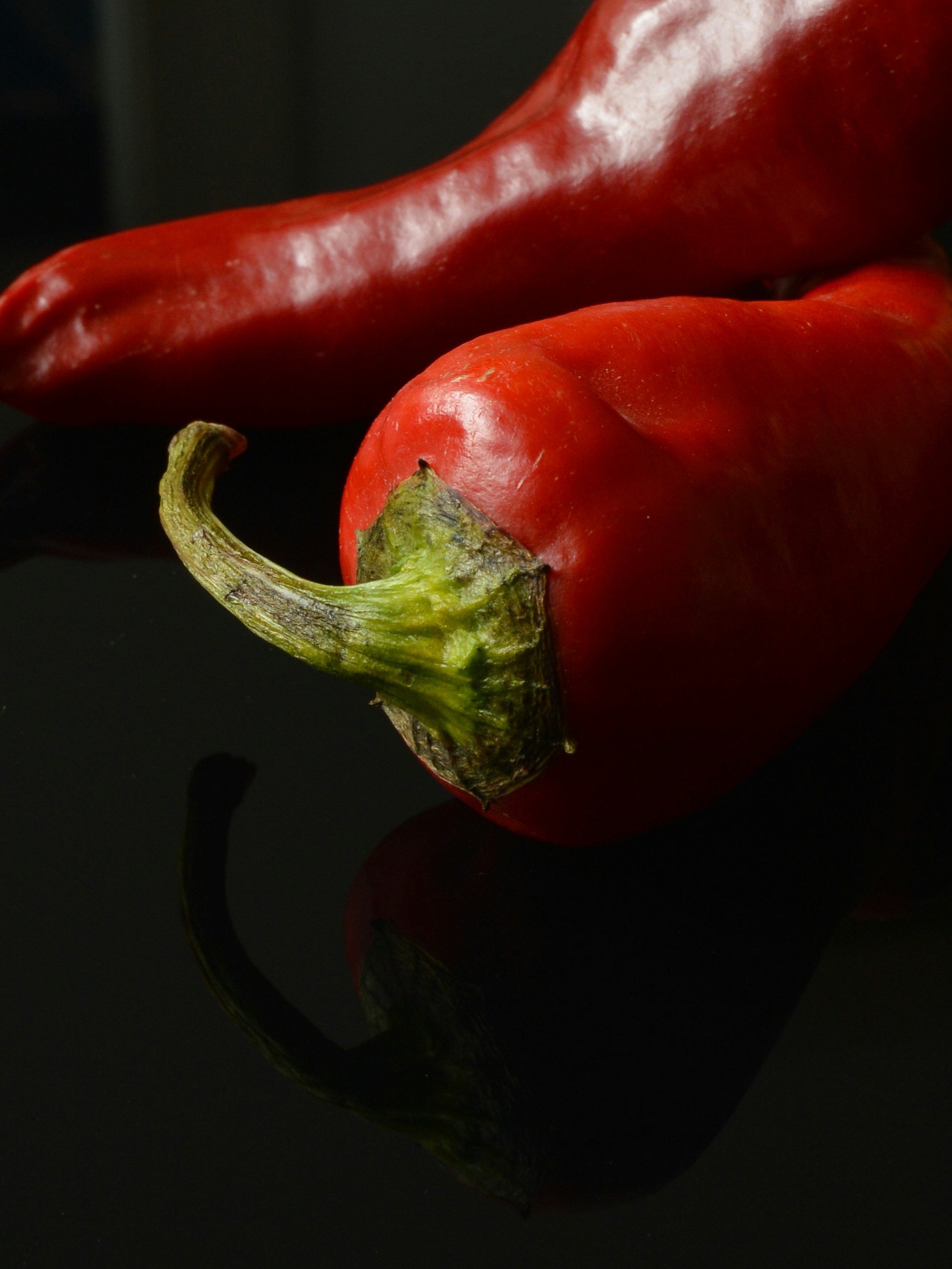 Two red chili peppers on a dark surface.