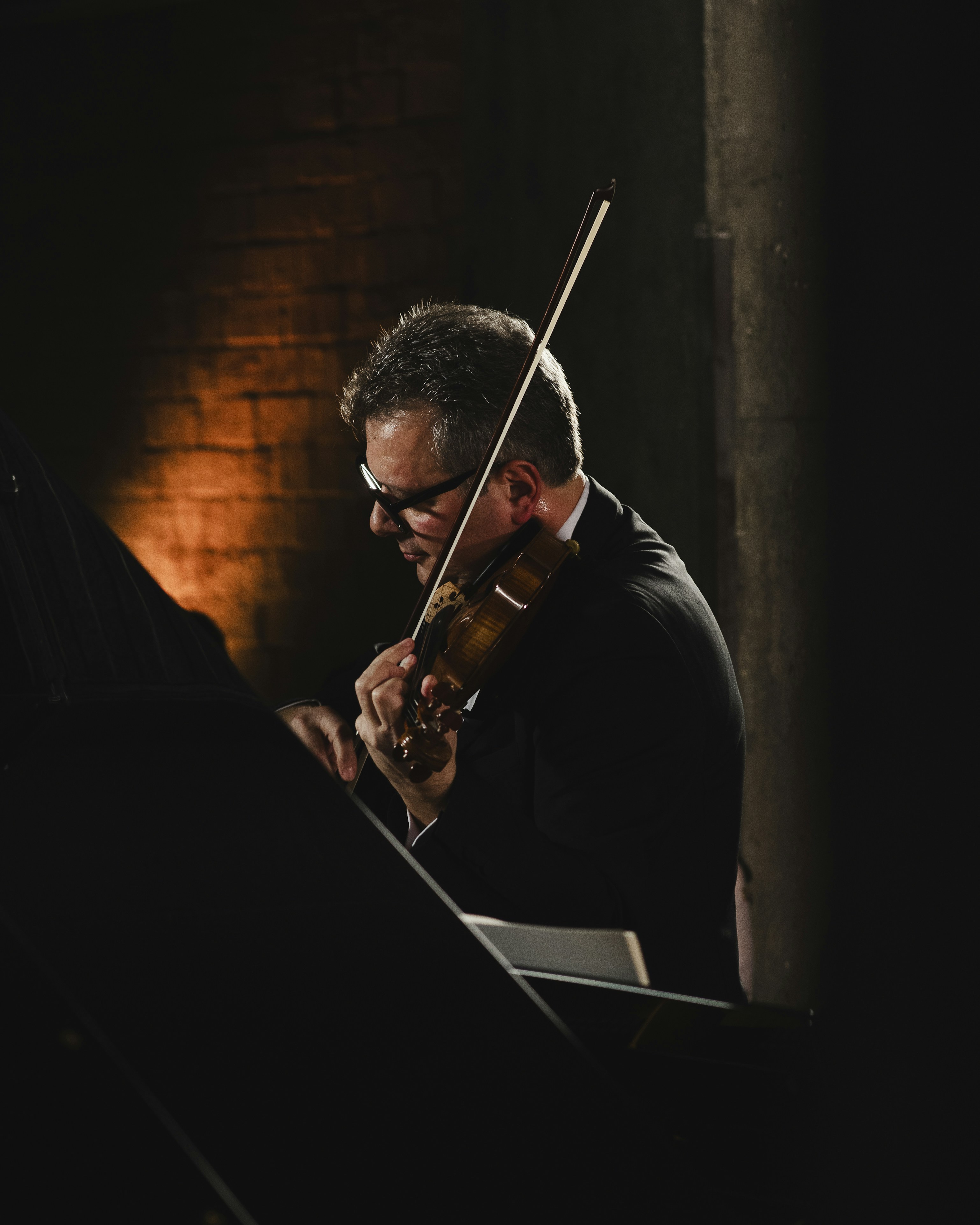 A young woman playing violin on a stage, viewed from the audience, with a spotlight on her.