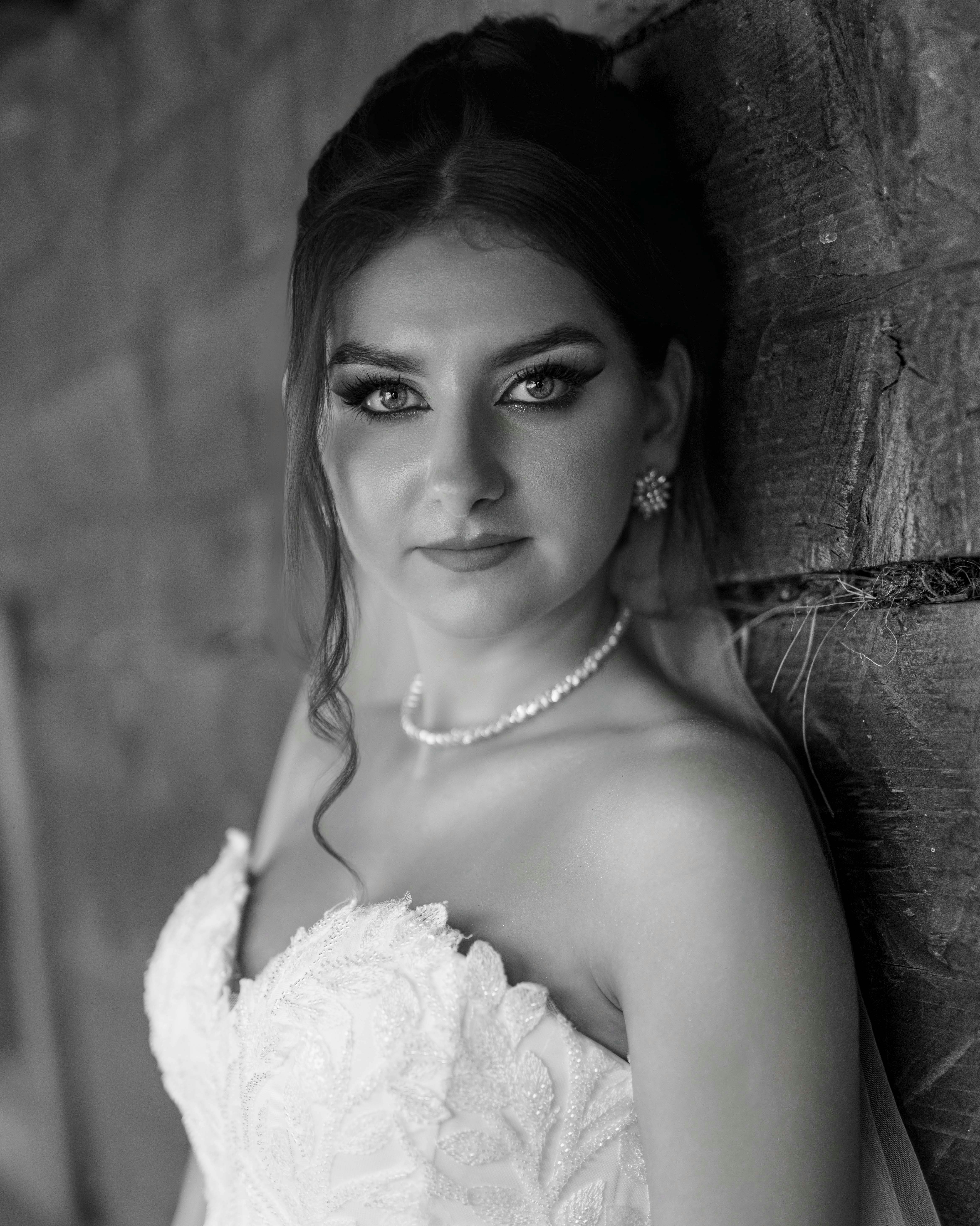 Braut im Hochzeitskleid, lehnt an der Holzwand.