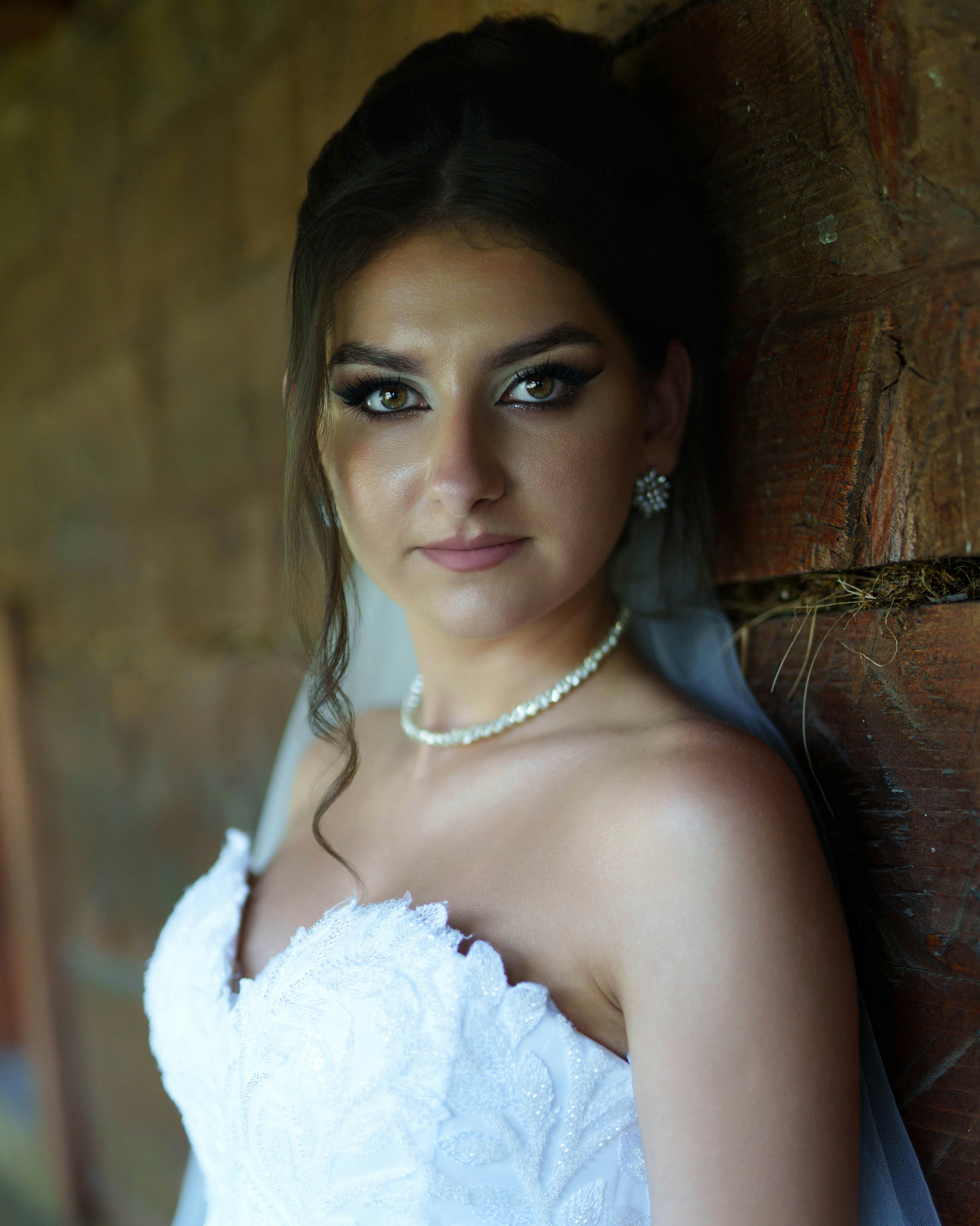 Braut im weißen Kleid, die an der Holzwand lehnt