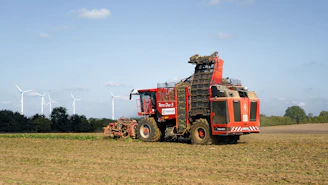 Red harvesting machine in a field with wind turbines.