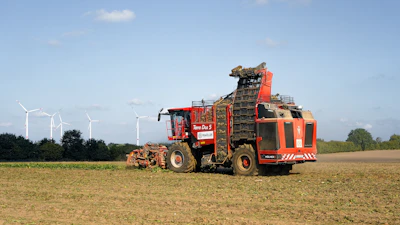 Red harvesting machine in a field with wind turbines.