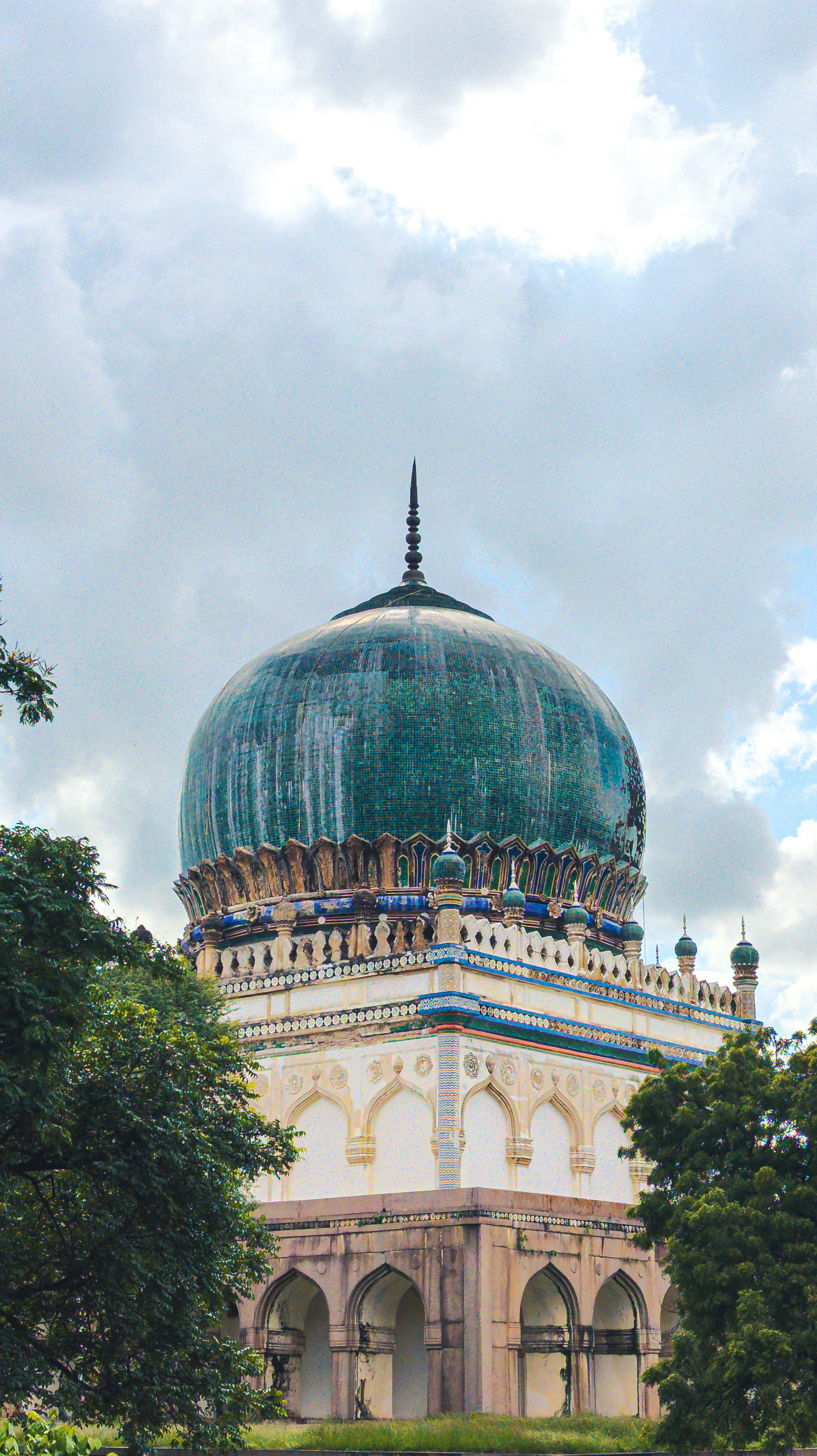A historic tomb with a green dome and arches.