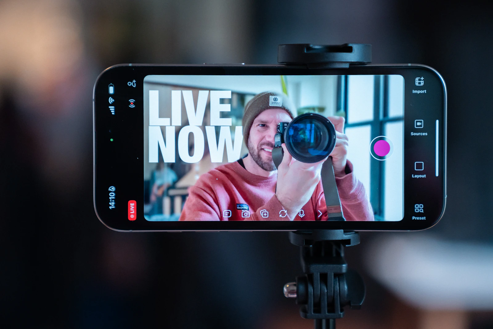 A smartphone on a tripod showing a creator filming himself, with the room blurred behind