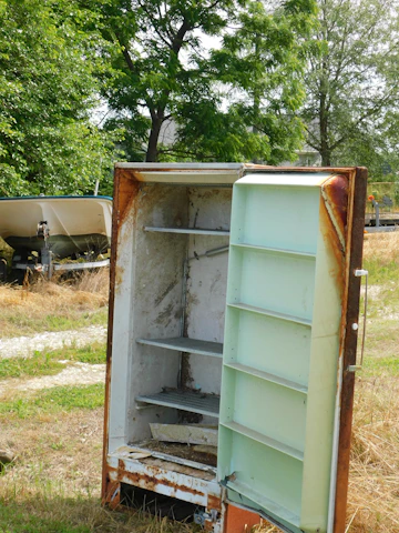 Old rusty refrigerator standing outdoors in grass