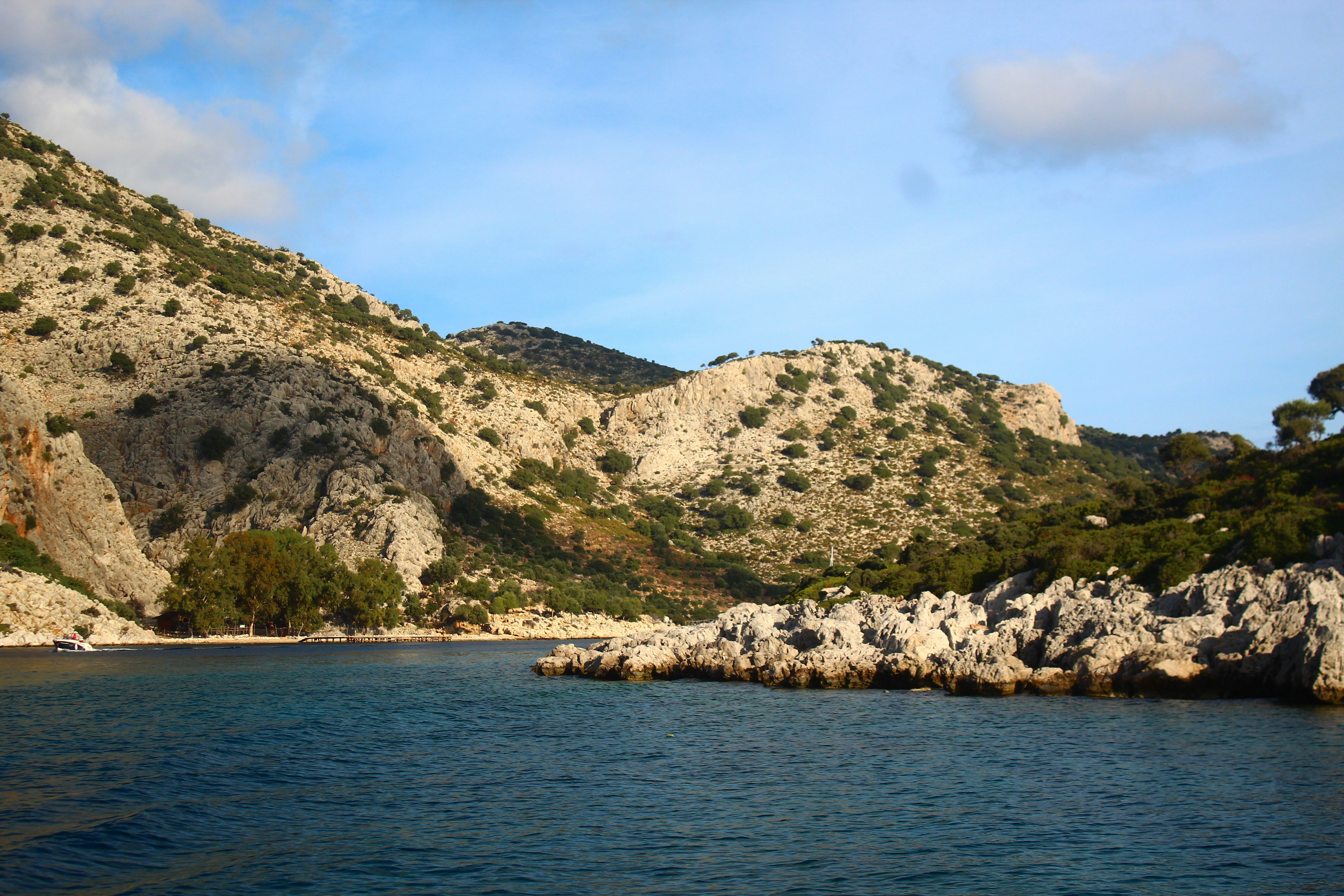Rocky coastline with calm blue water and hills.