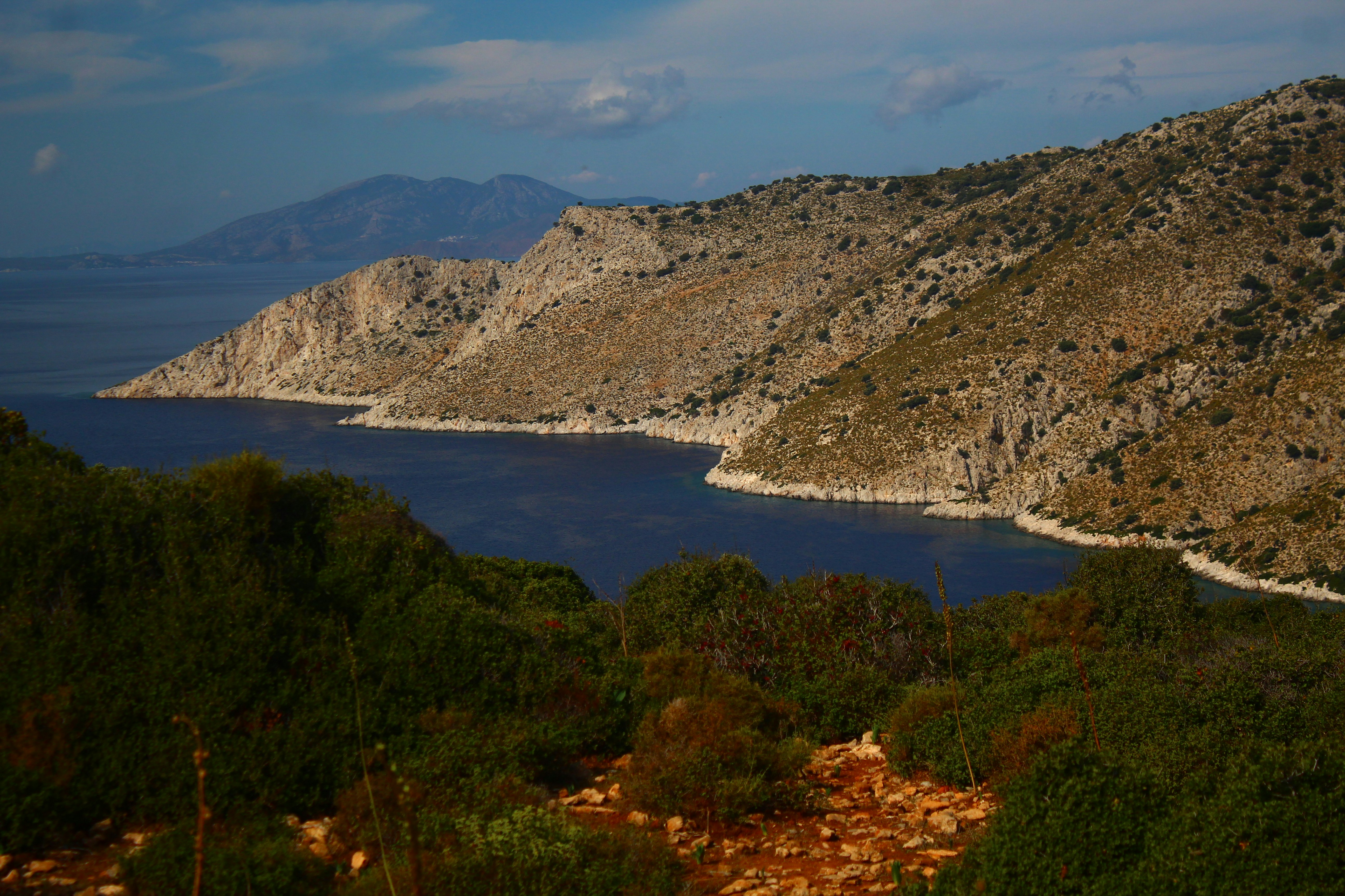 Rocky coastline with calm blue water and distant mountains.