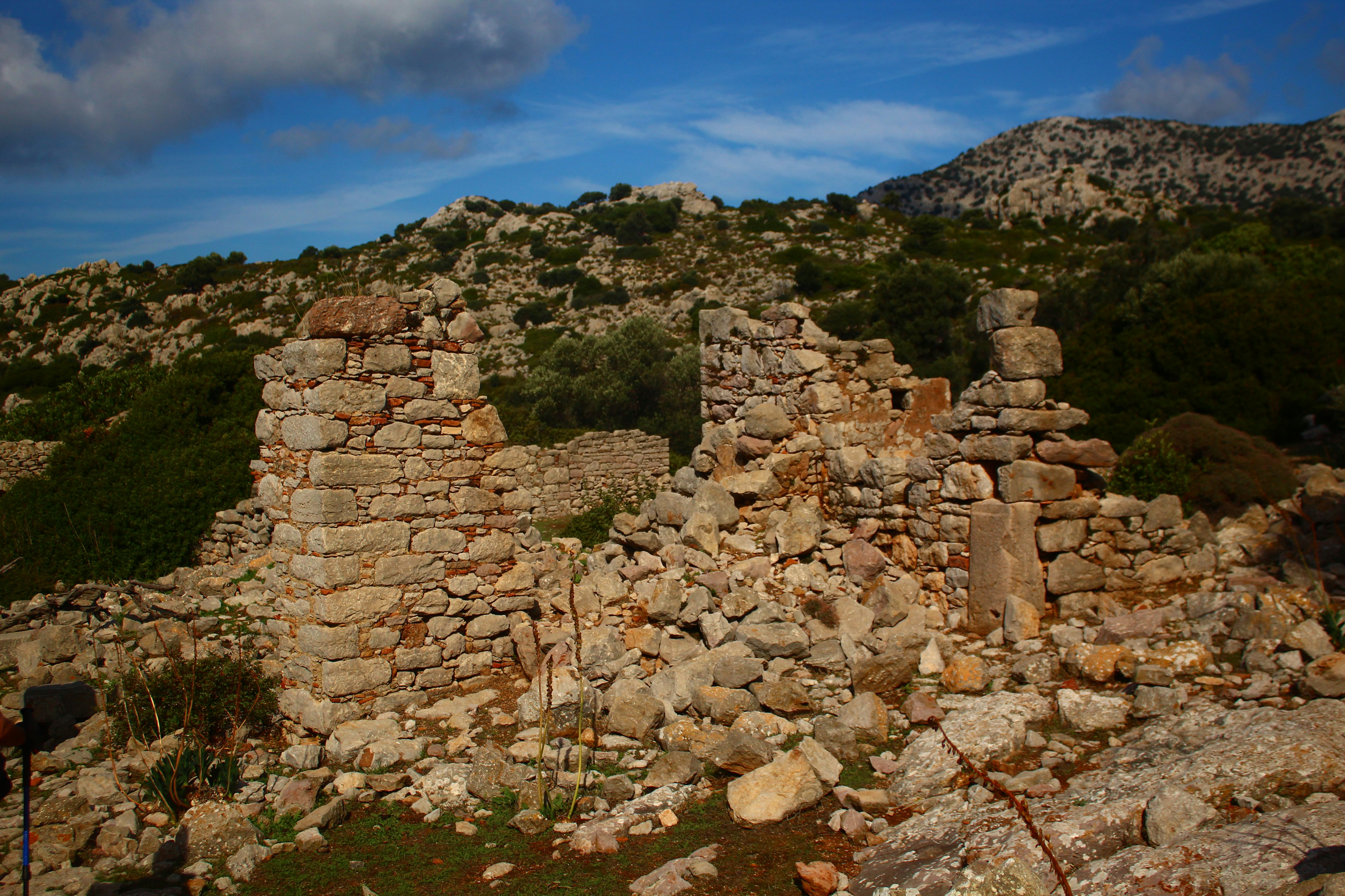 Ancient stone ruins on a rocky hillside under blue sky.