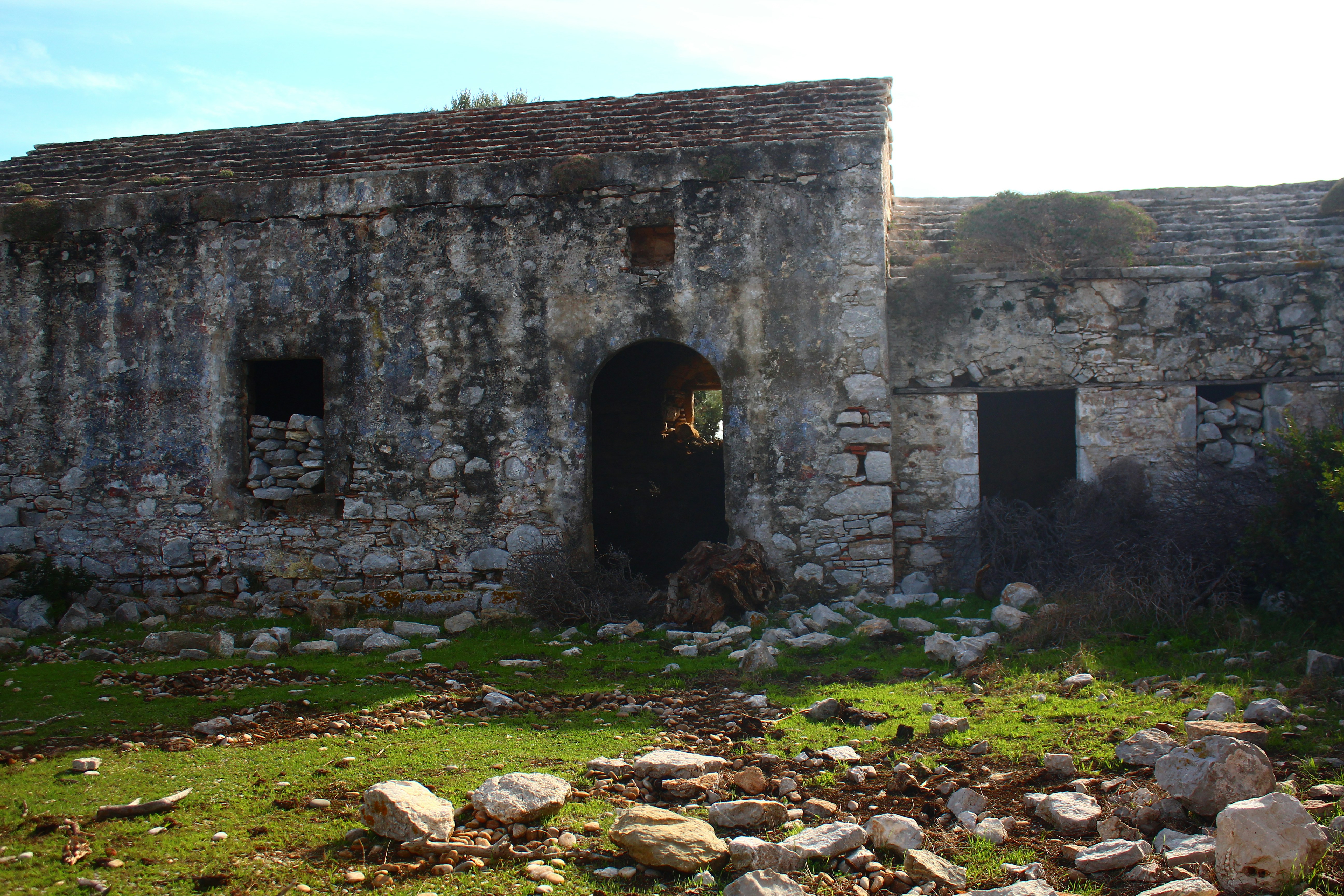 Old stone building with arched doorway and overgrown vegetation.