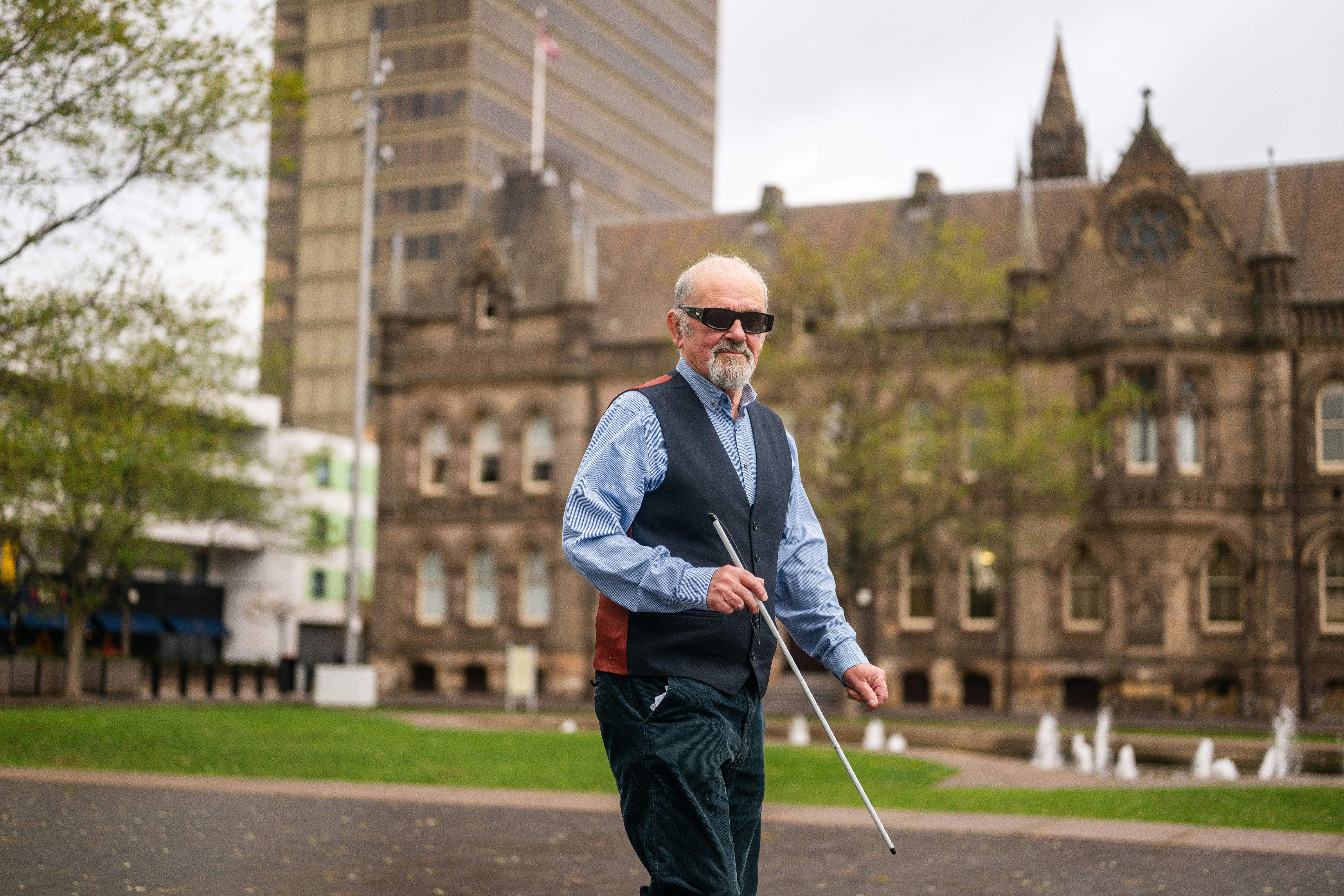 Elderly blind man walking with a white cane.